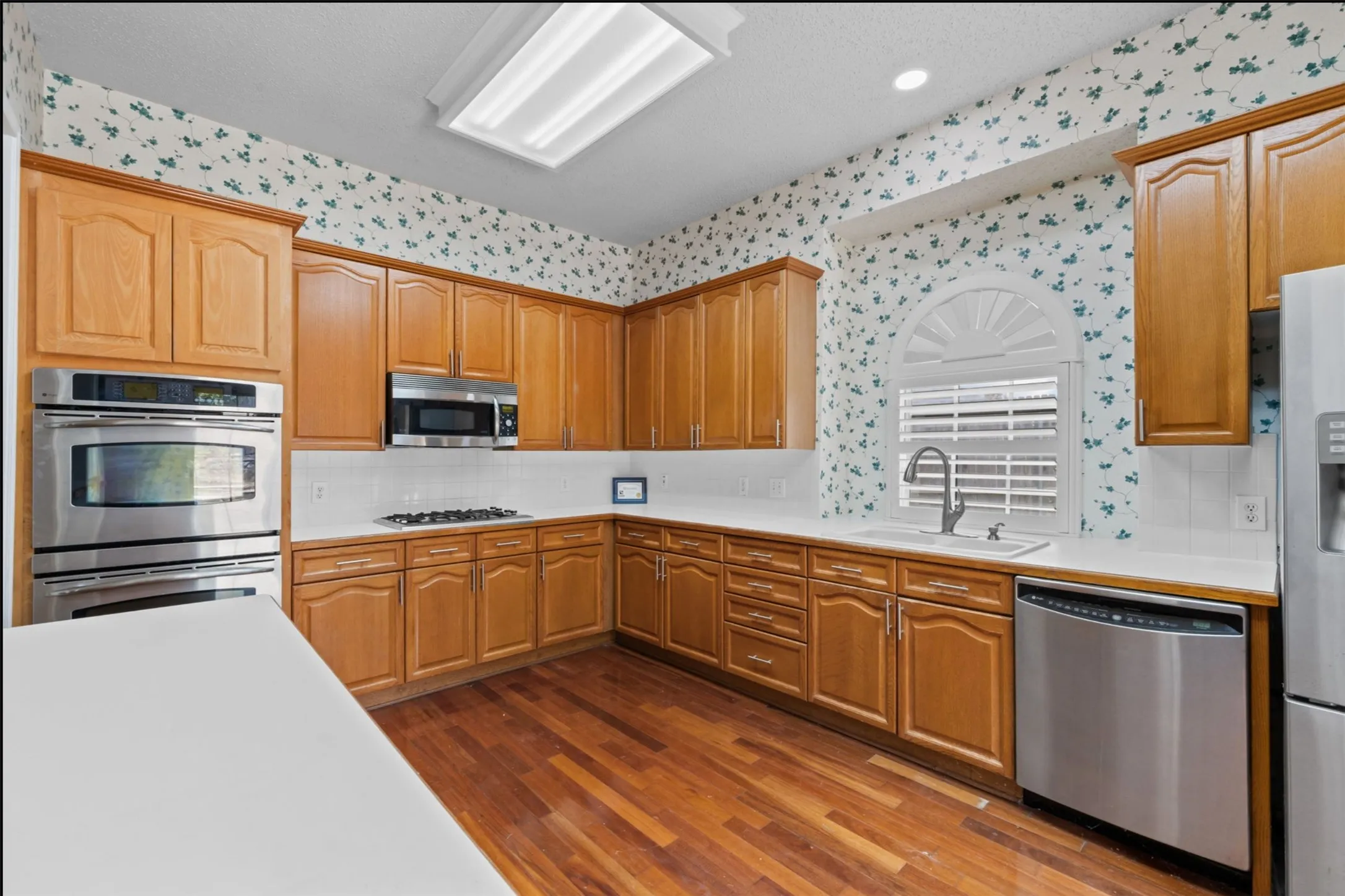 Kitchen featuring wood flooring, light wood cabinetry, white countertops, stainless steel appliances, and a gas range