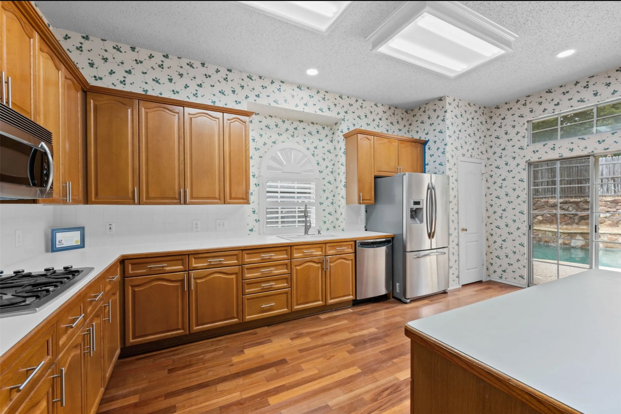 Wood flooring, ample wood cabinetry, white countertops, built-in stainless steel appliances, and a sliding glass door, pantry