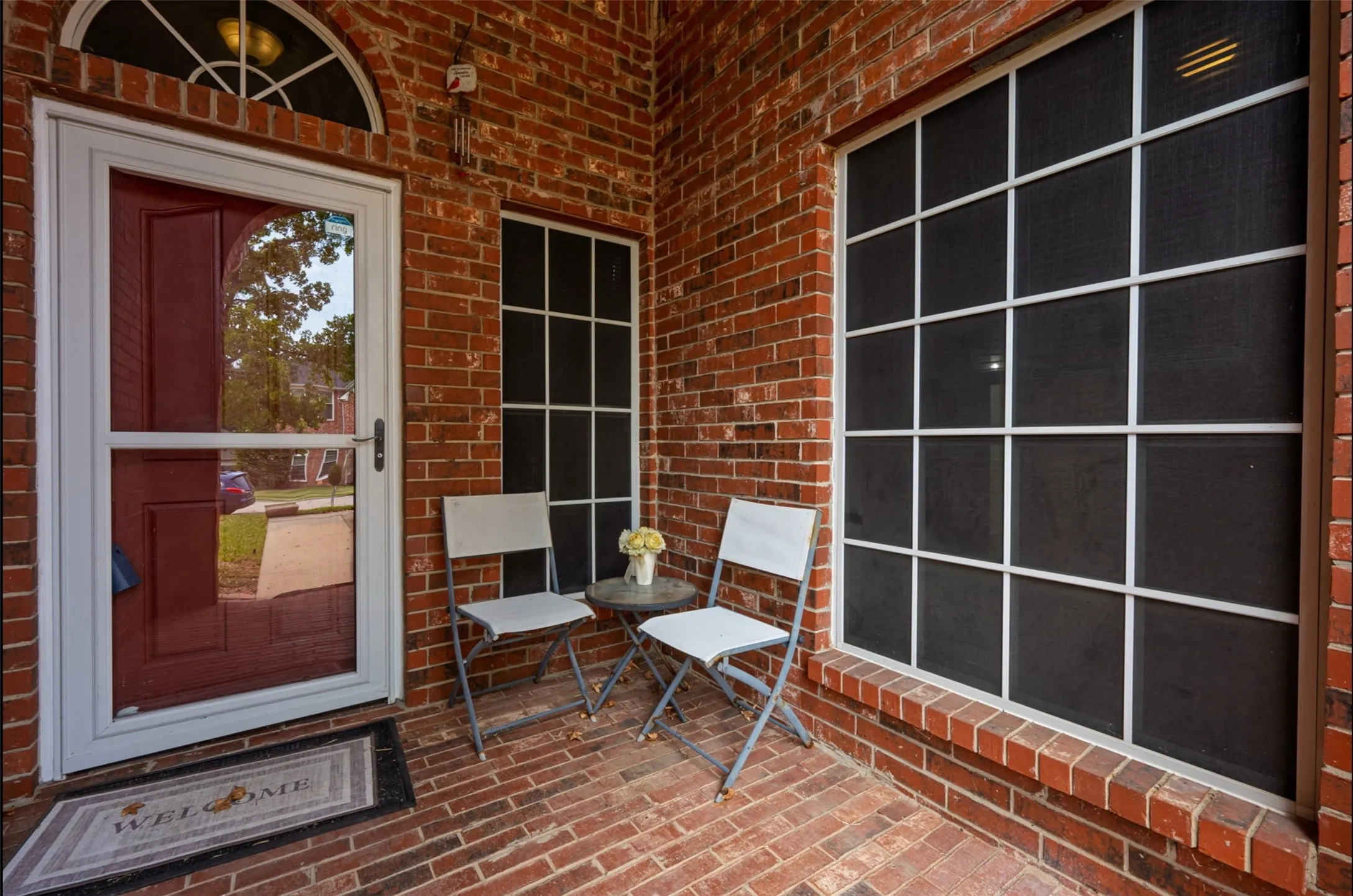 Brick exterior with a covered porch and solar screens featuring a security screen door, an arched transom window, and a large multi-pane grid look window