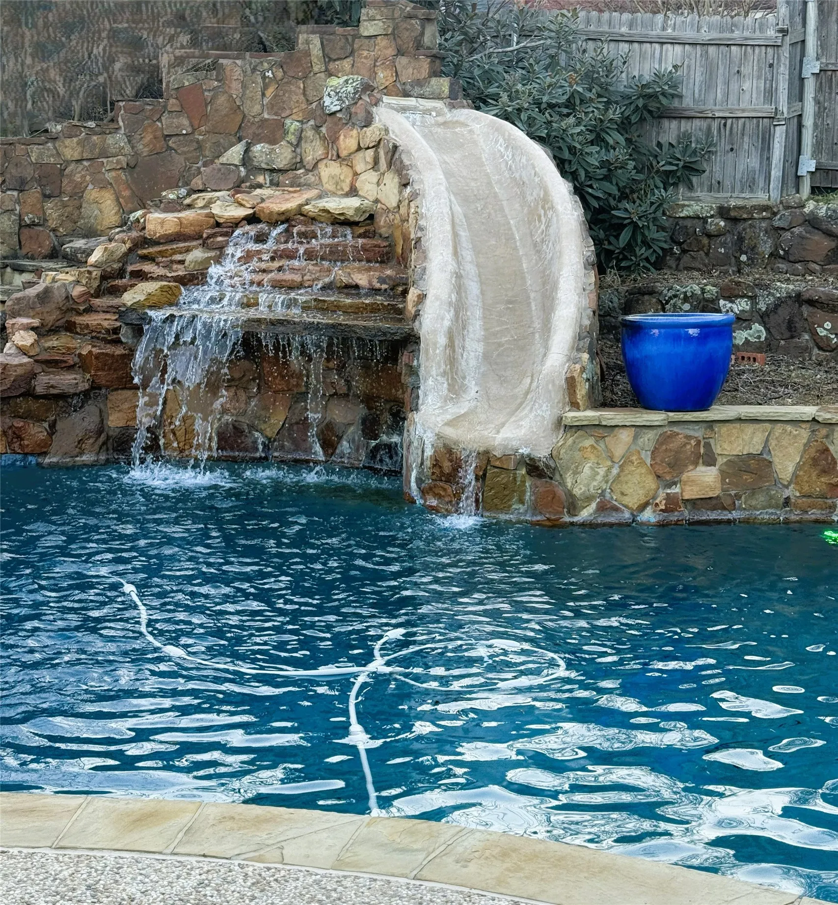 Pool with a stone waterfall feature, integrated slide, and stone coping