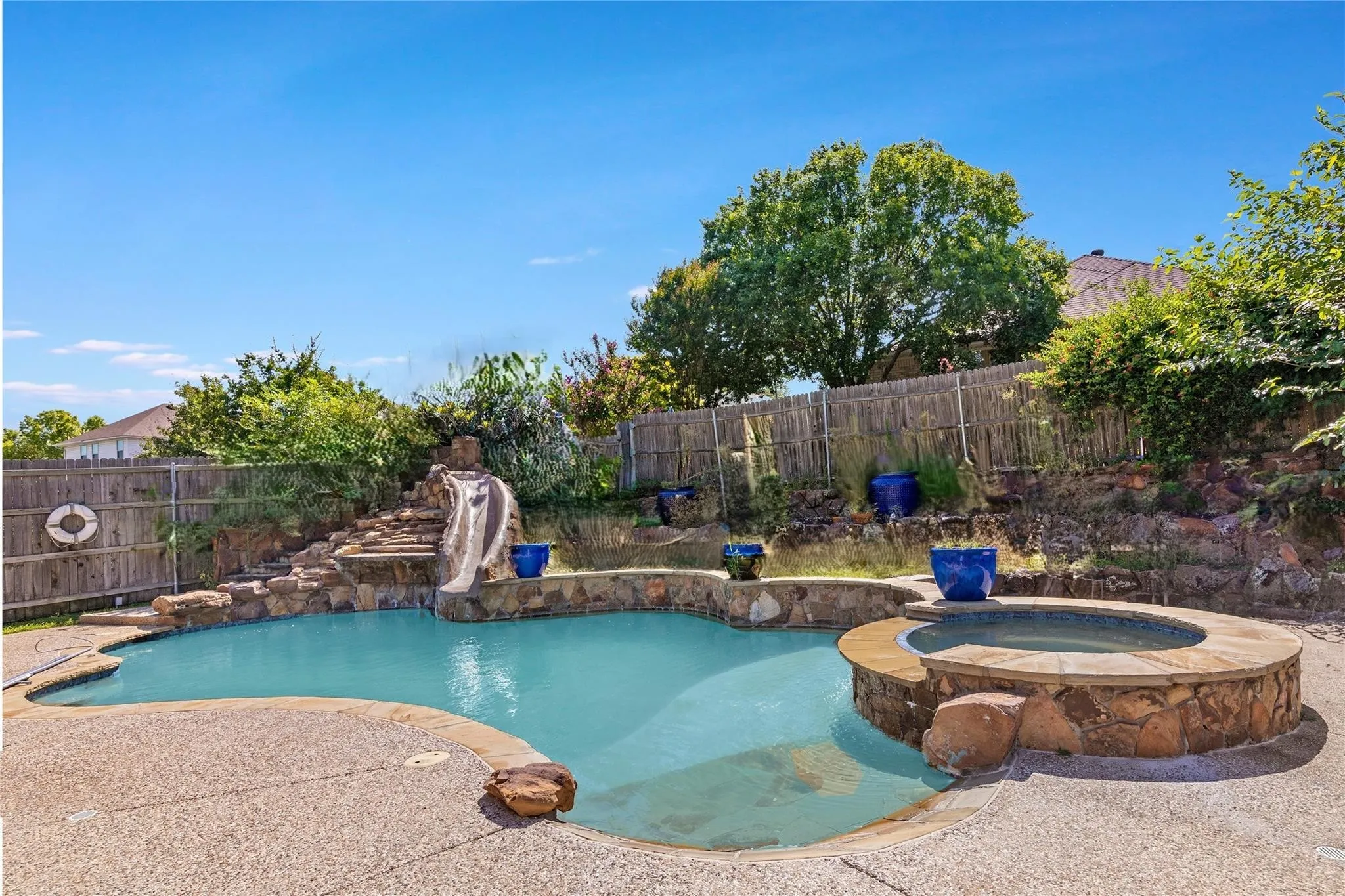 Custom-shaped swimming pool with an integrated spa, stone-clad water slide, and rock accents