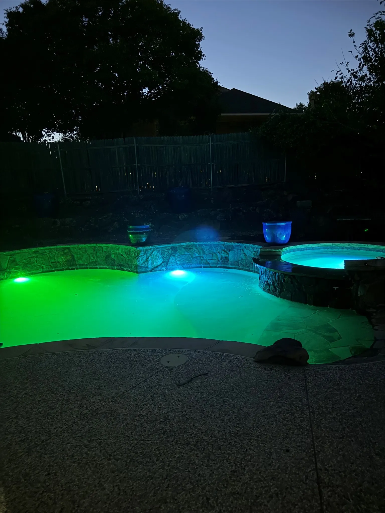 Illuminated swimming pool with an integrated spa, stone coping, and a surrounding aggregate patio