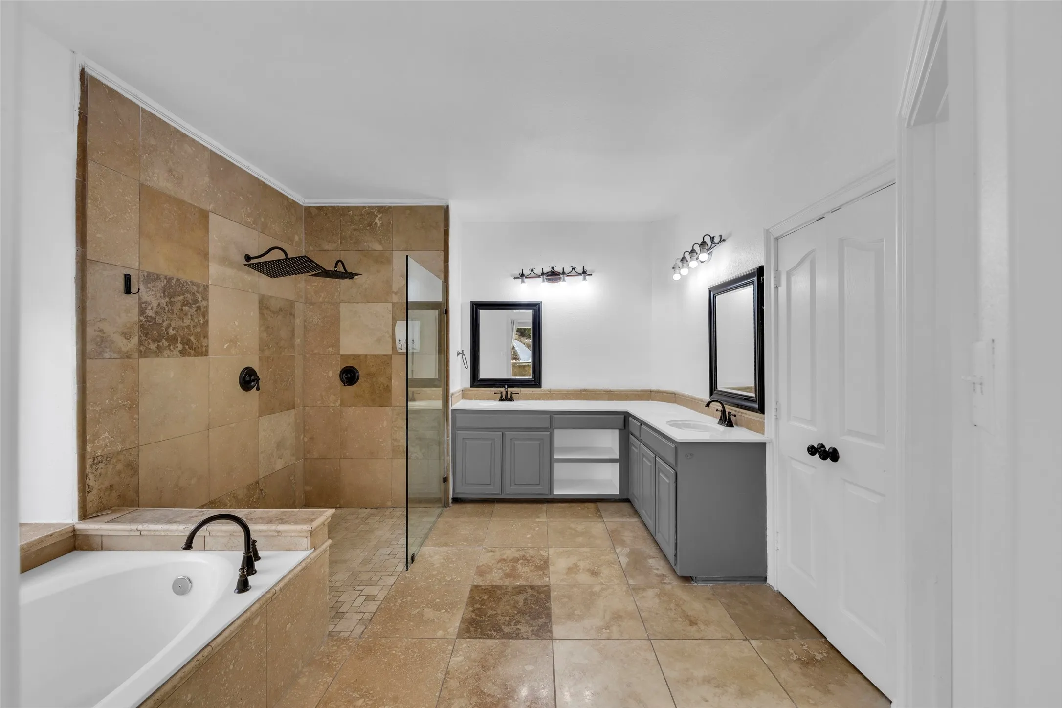 Spacious bathroom featuring a built-in soaking tub, a walk-in shower with tile surround and glass enclosure, dual vanity with solid surface countertops, and tile flooring
