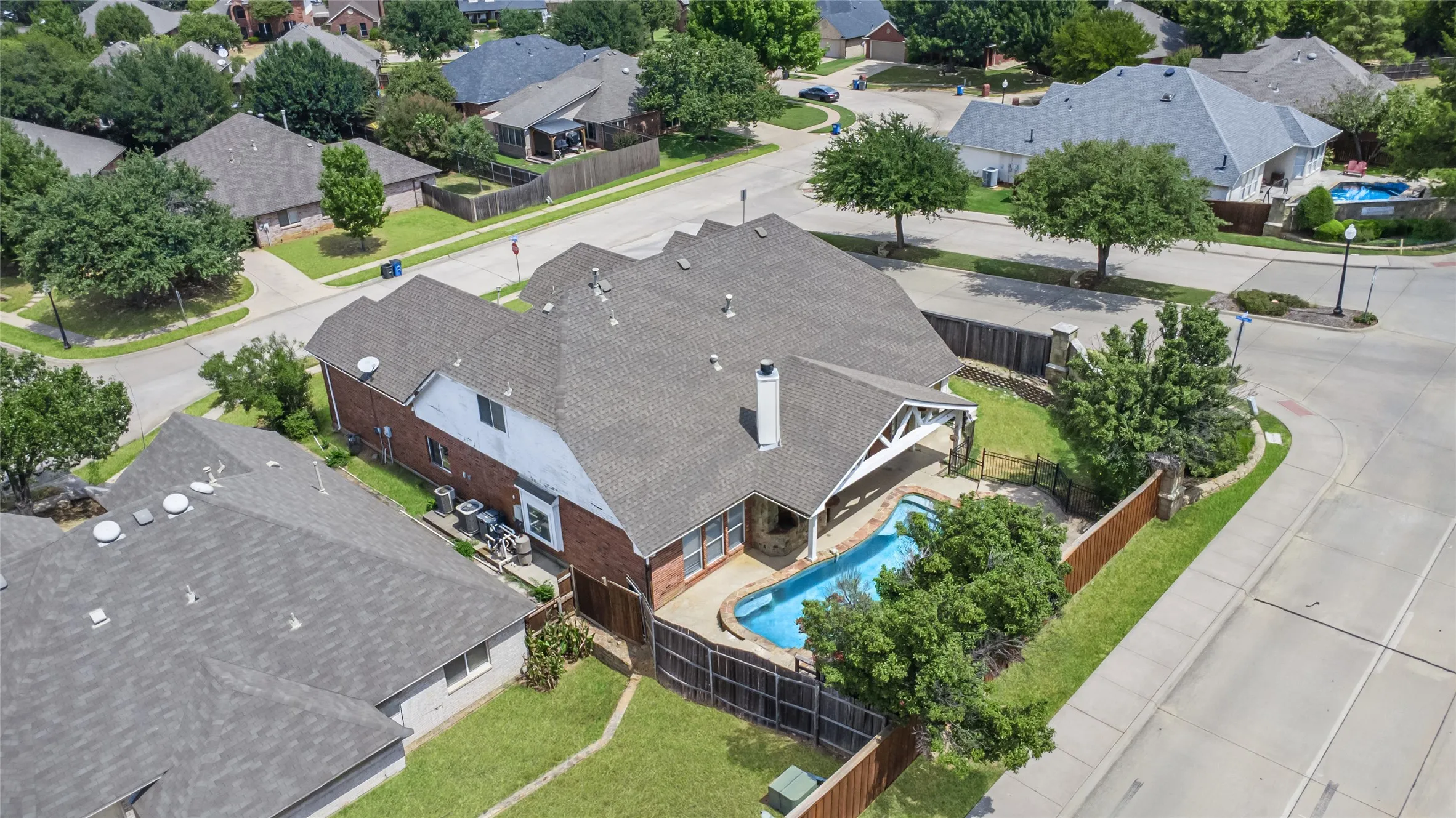 Brick exterior residence featuring a gray shingle roof, a backyard swimming pool, and a covered patio