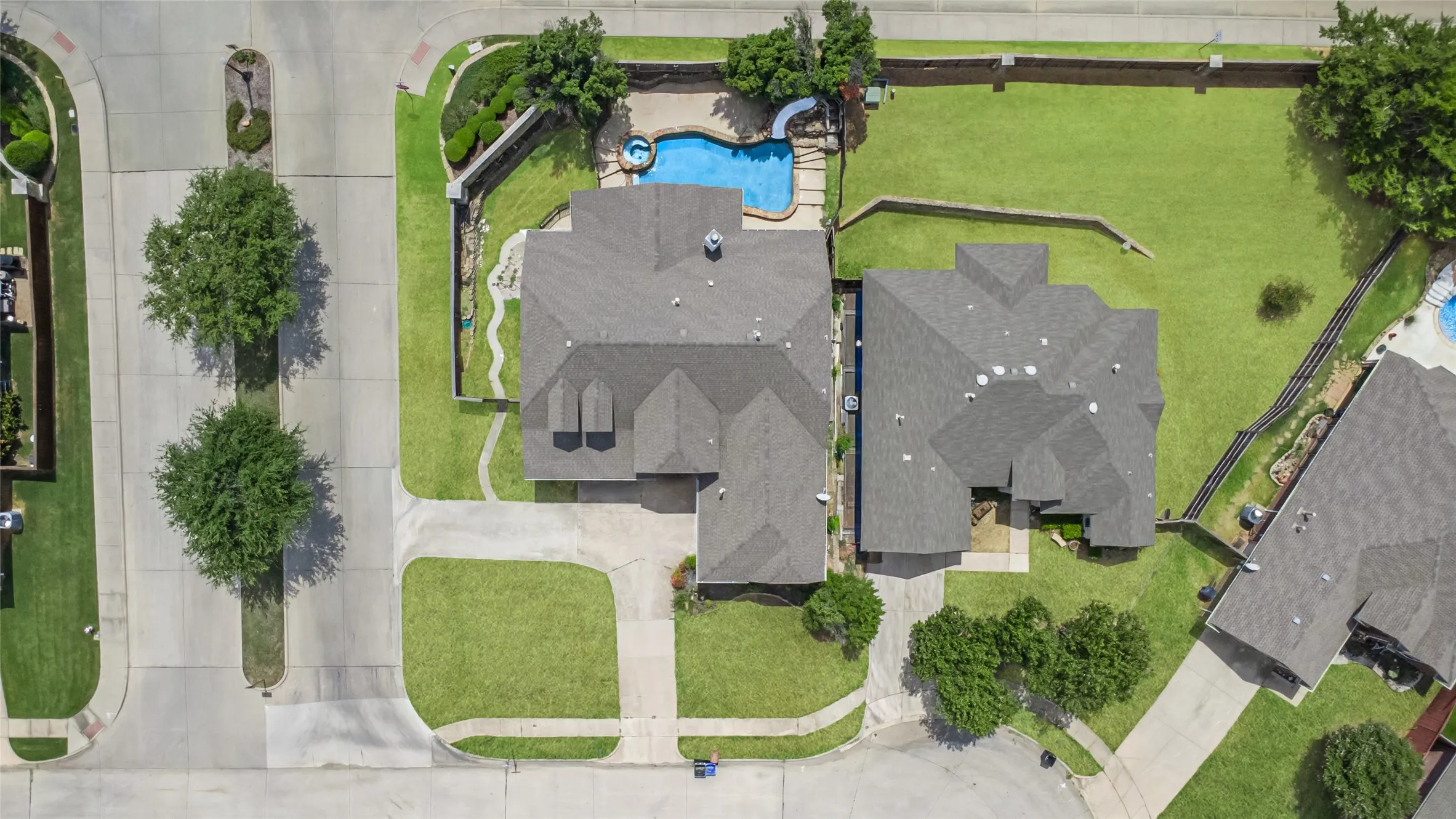Asphalt shingle roof, expansive green lawn, concrete driveway, stone retaining wall, and an in-ground swimming pool