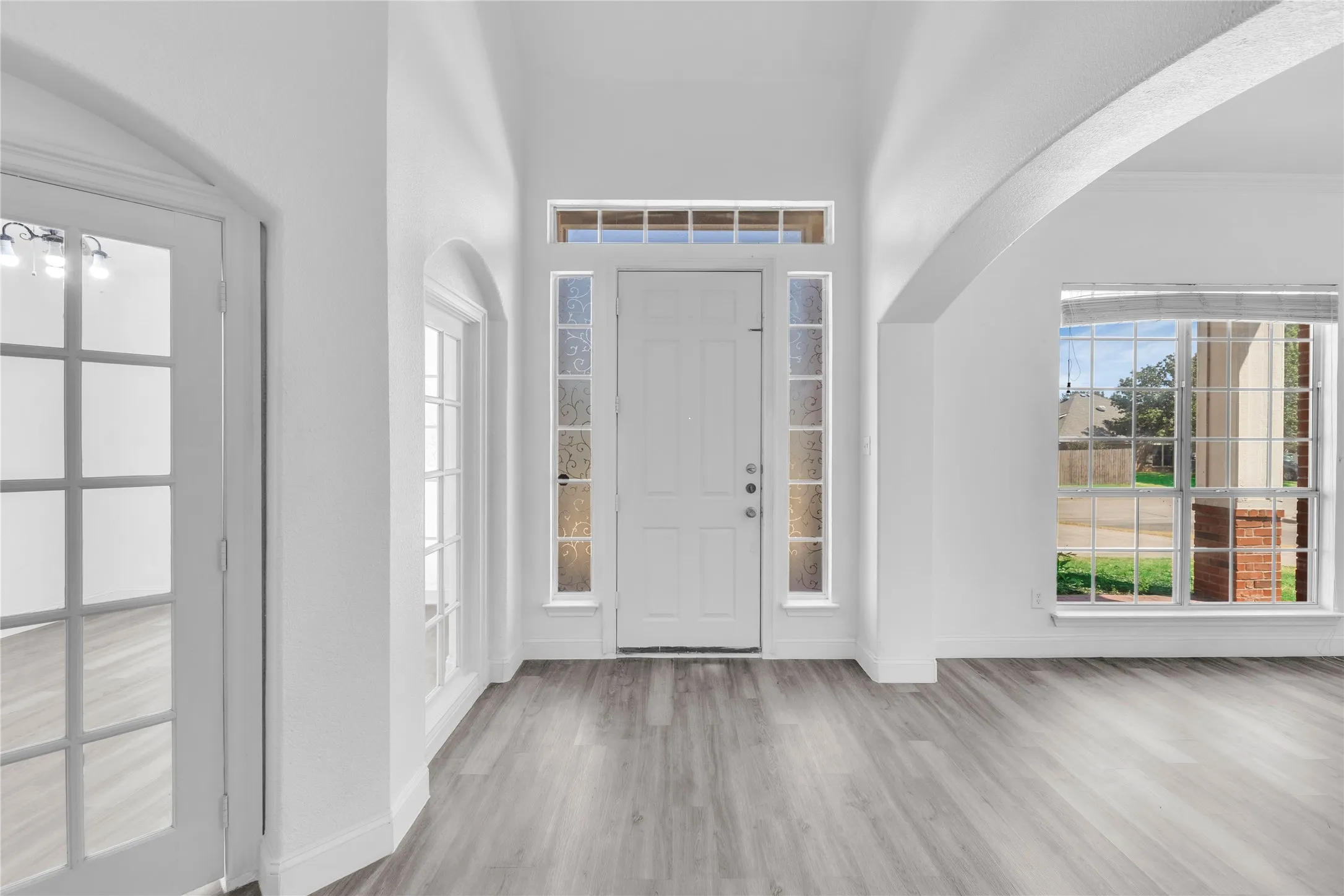 Entryway featuring wood-finish flooring, a transom window, sidelight windows, and an arched doorway