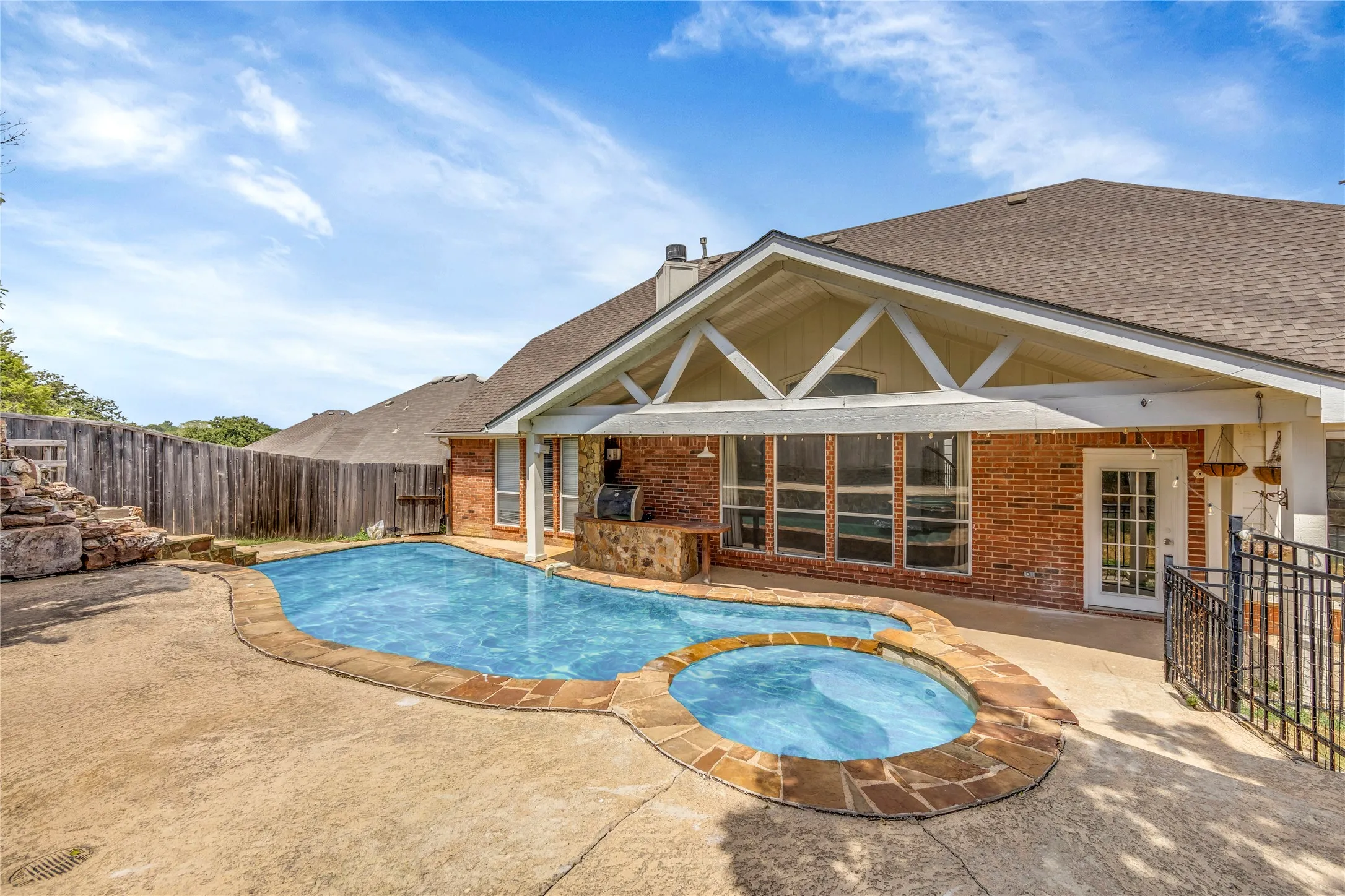 Brick exterior with a covered patio, a built-in outdoor cooking area, a swimming pool, an integrated spa, and a stone water feature