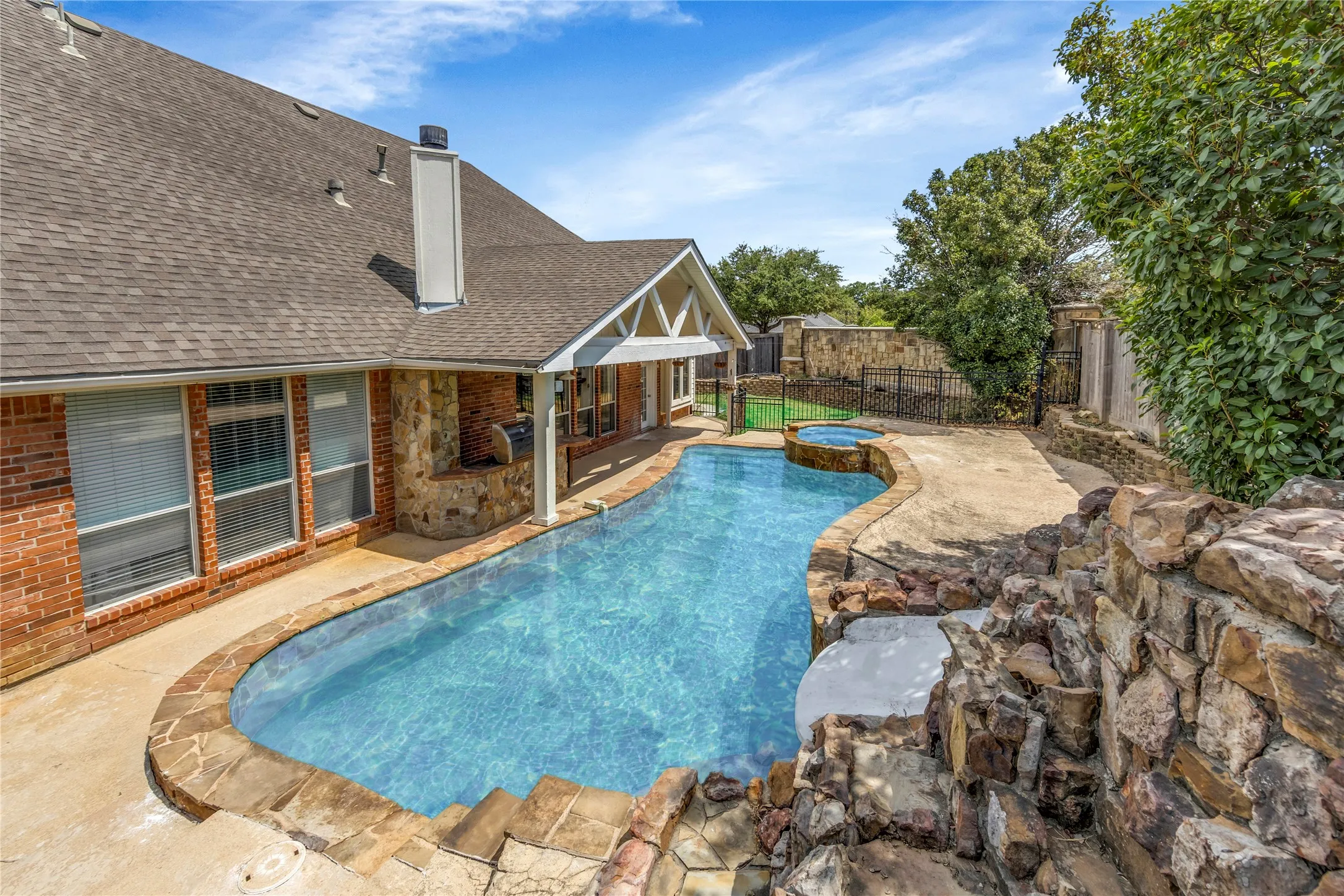 Outdoor swimming pool with stone coping and integrated spa, complemented by a rock waterfall feature