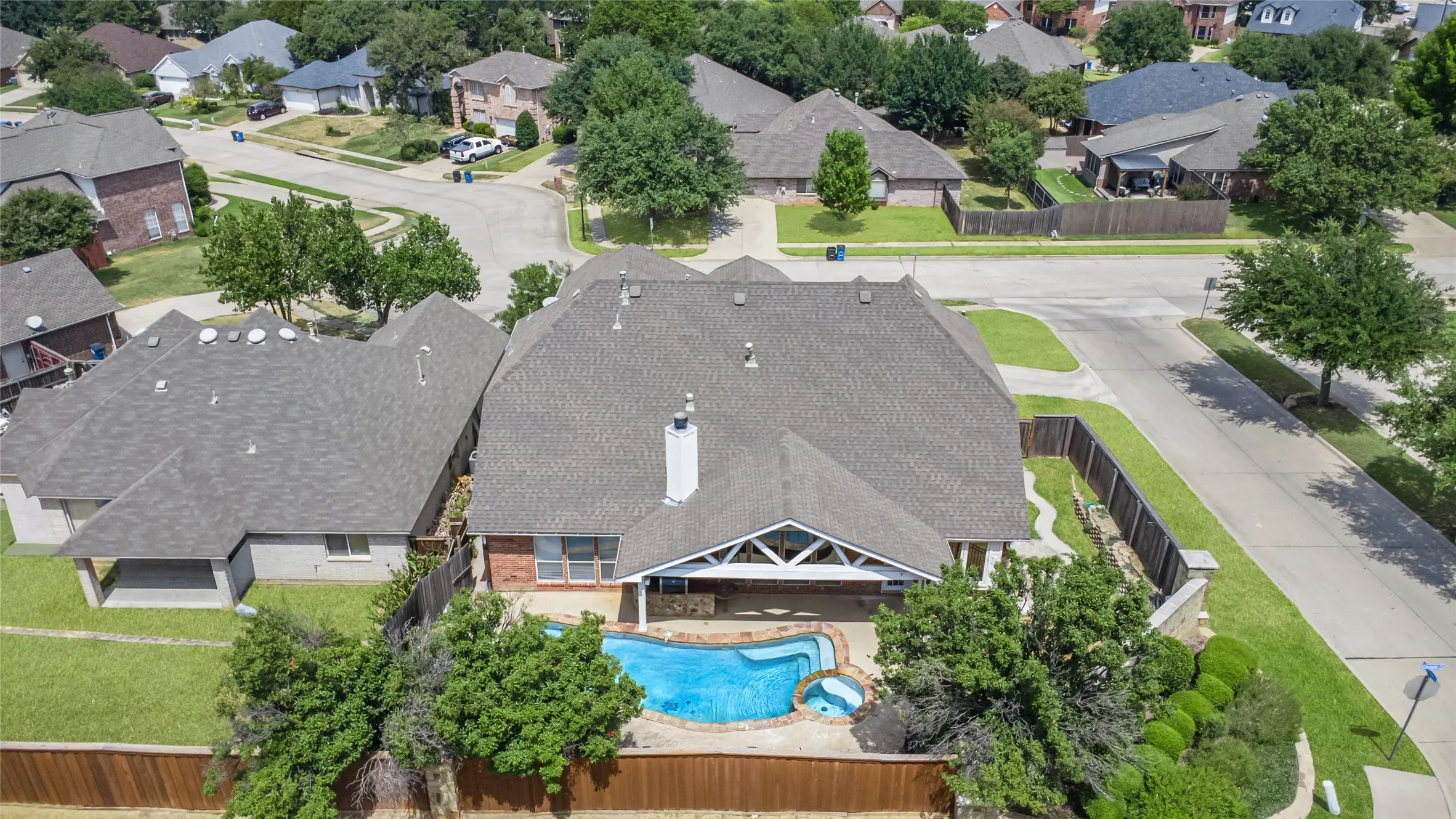 Brick exterior home with a shingled roof, featuring a built-in swimming pool with an attached spa