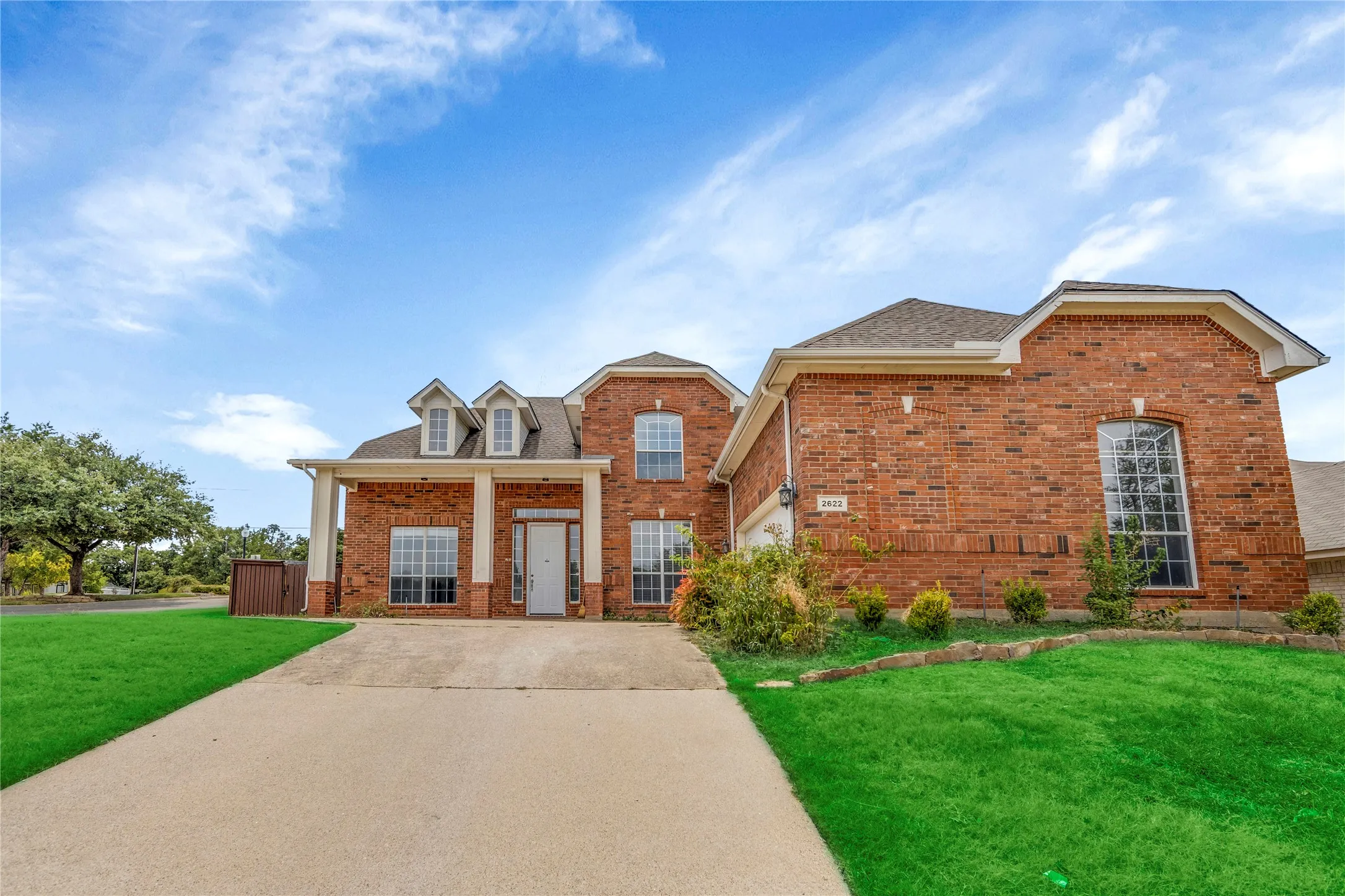 Brick facade, multi-gabled roofline, front-facing dormer windows, covered entry with columns, arched window