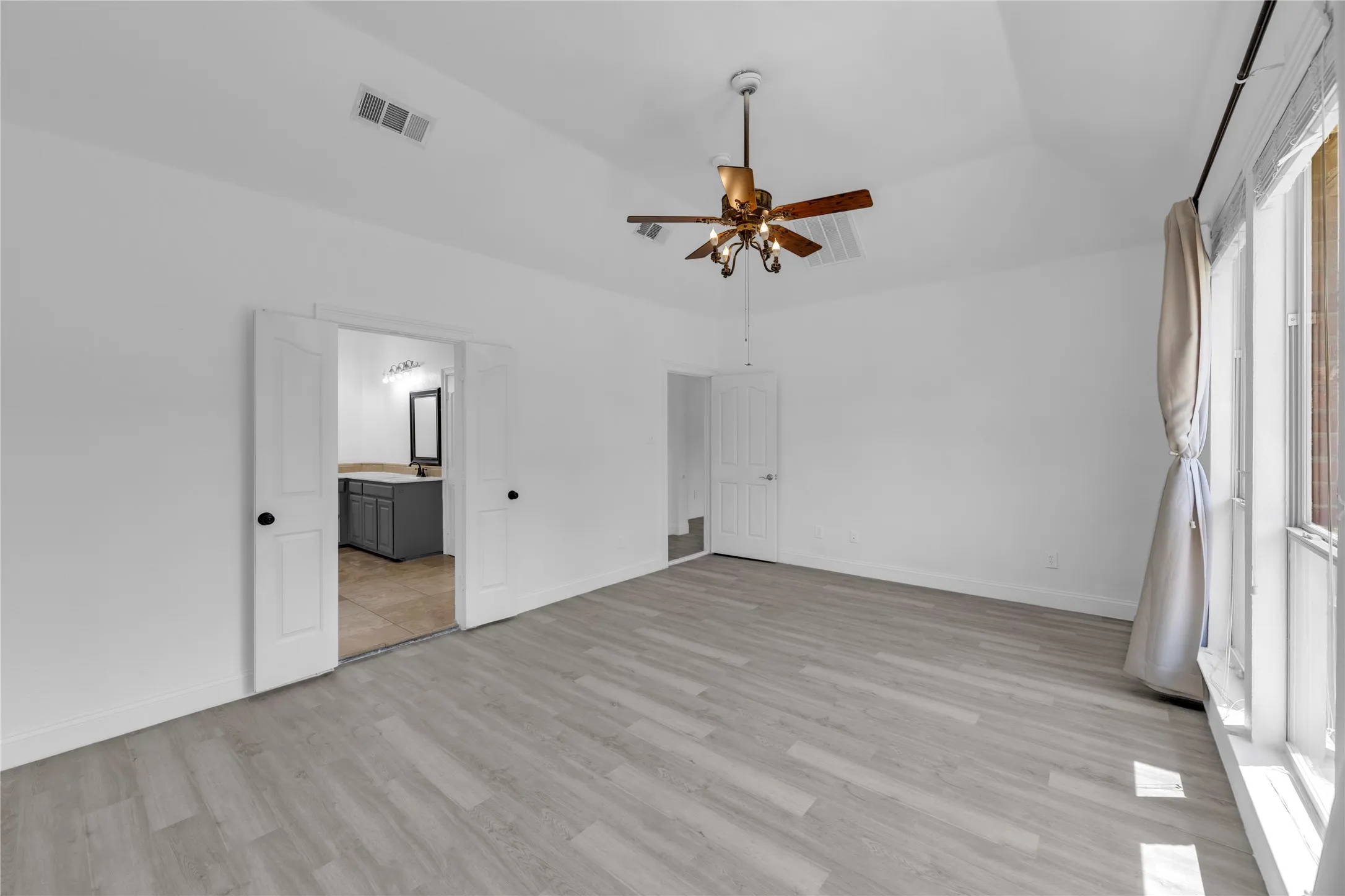 Vaulted ceiling featuring a ceiling fan, wood-finish flooring, white double doors, and an additional door