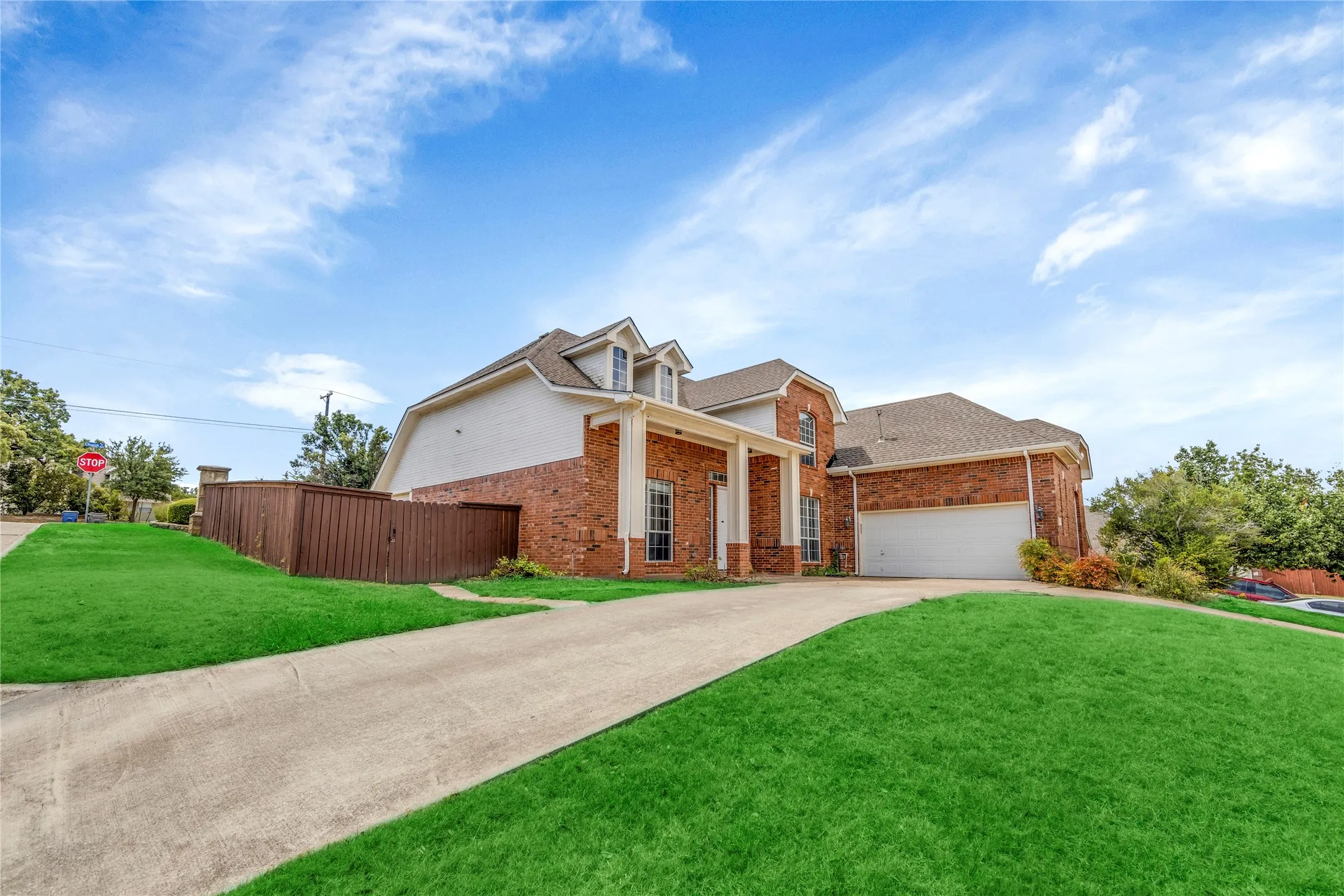 Brick exterior with white trim, columned front entry, dormer windows, attached garage, and concrete driveway