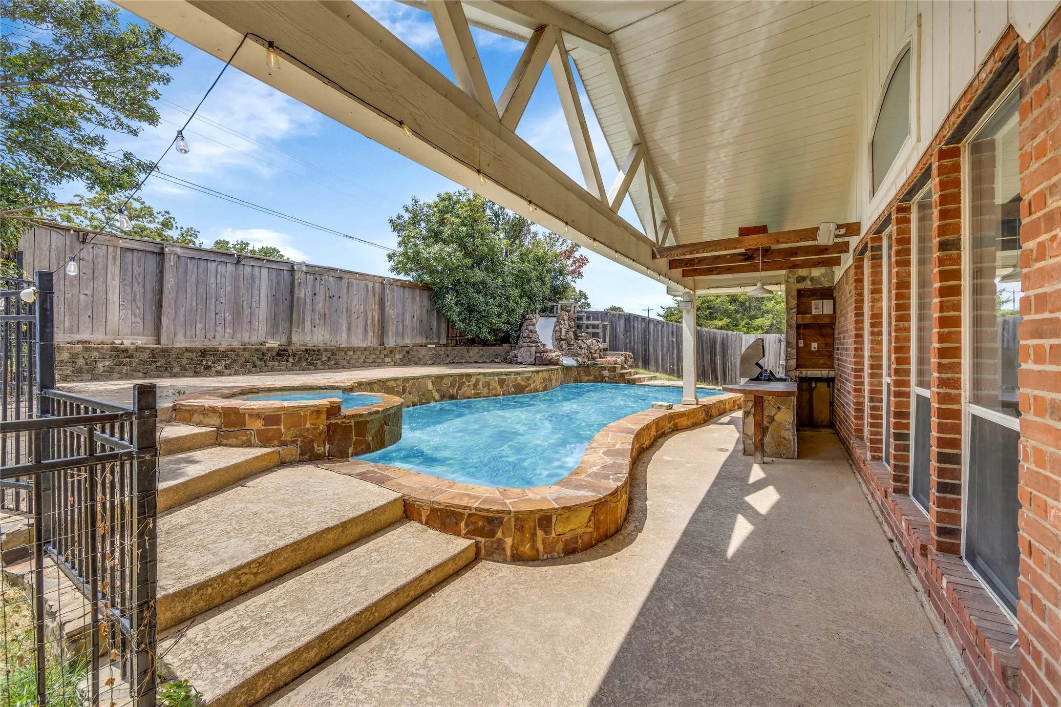 Covered patio with integrated outdoor cooking station, brick exterior, and multiple large windows