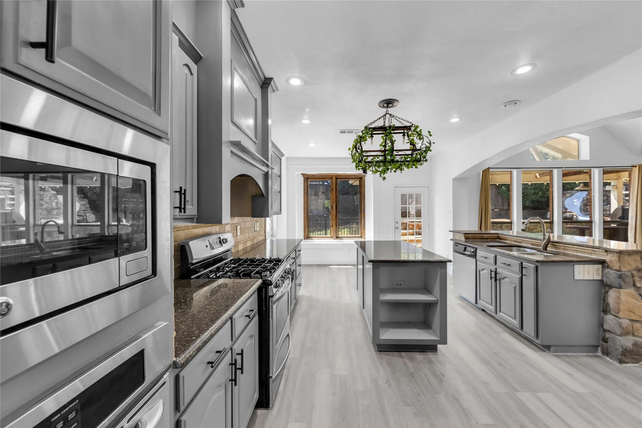 Kitchen featuring light grey cabinetry, stainless steel appliances, dark countertops, and light wood-finish flooring
