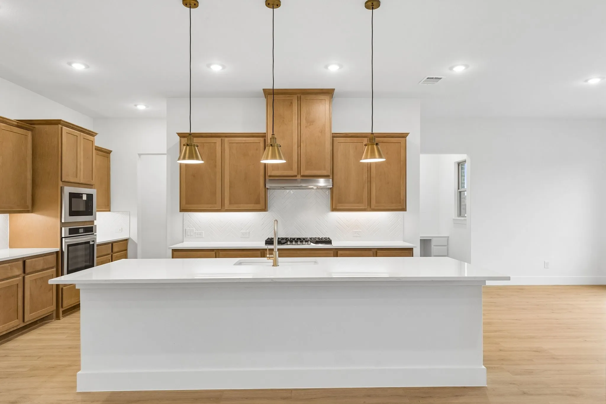 Central island with an integrated sink, natural wood cabinetry, stainless steel appliances, pendant lighting, and recessed ceiling lights