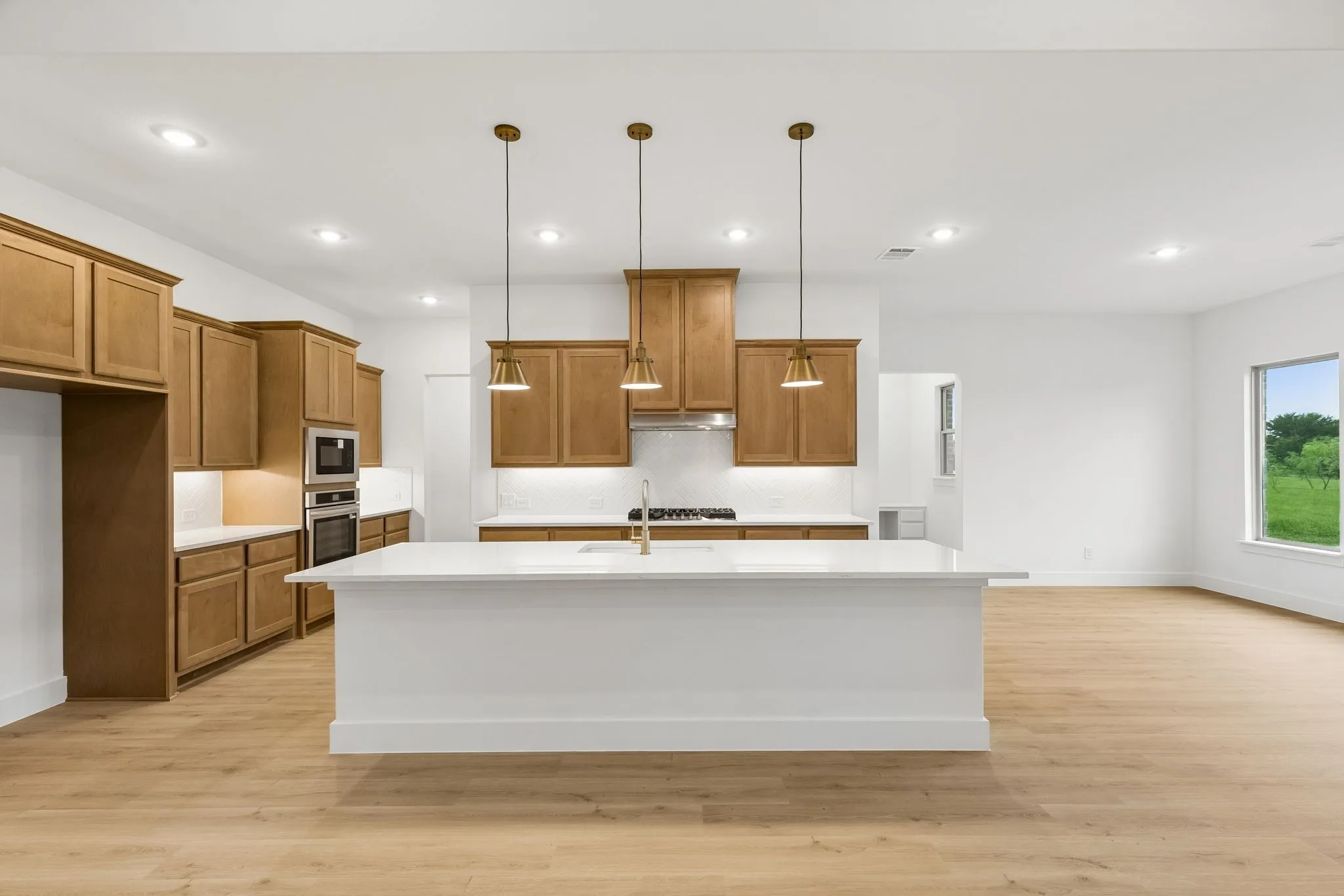 Kitchen featuring a large island with white countertops, light wood-finish flooring, built-in stainless steel appliances, and wood cabinetry