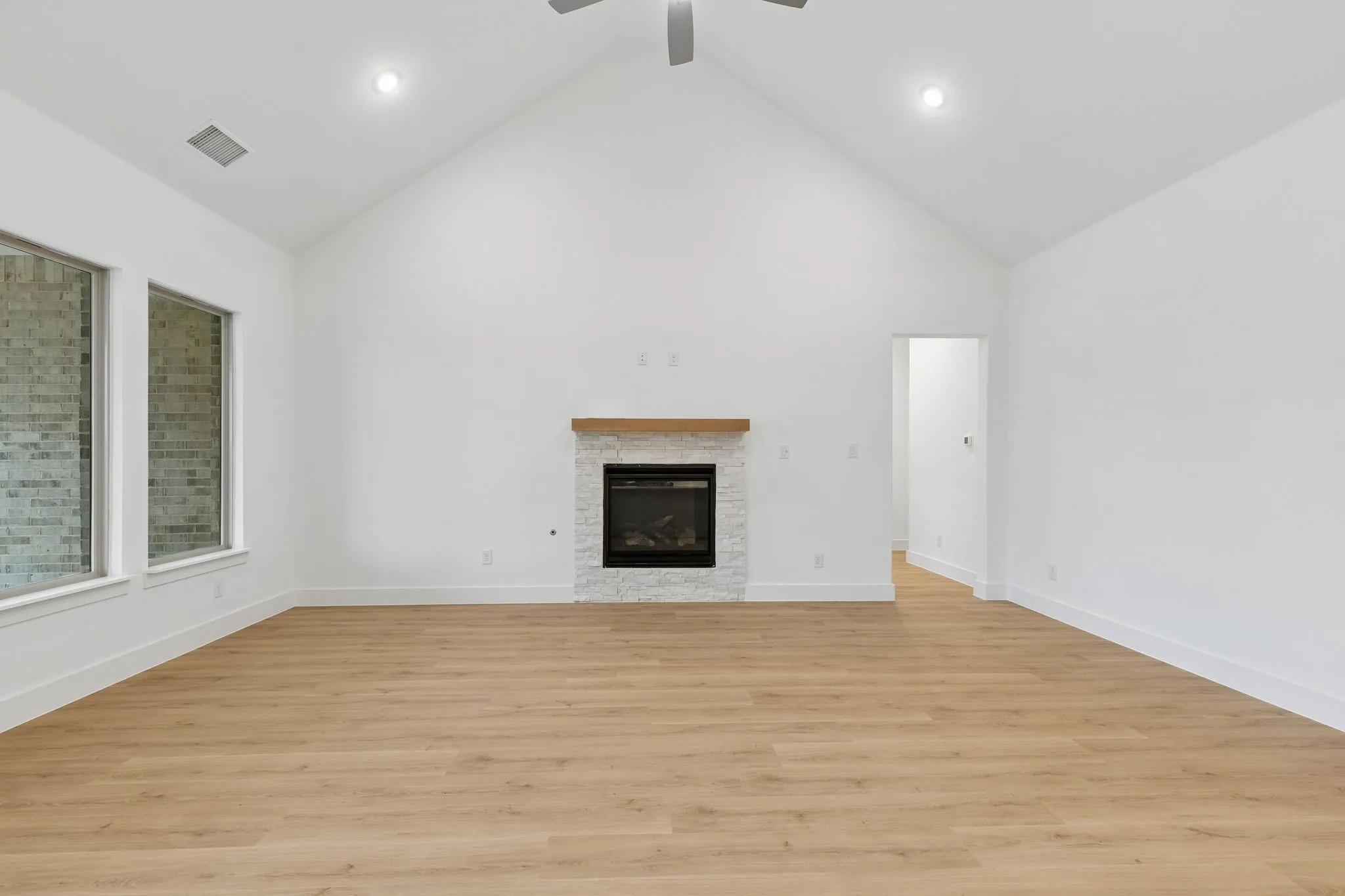 Vaulted ceiling, wood-finish flooring, fireplace with stone surround, wood mantel, and recessed lighting