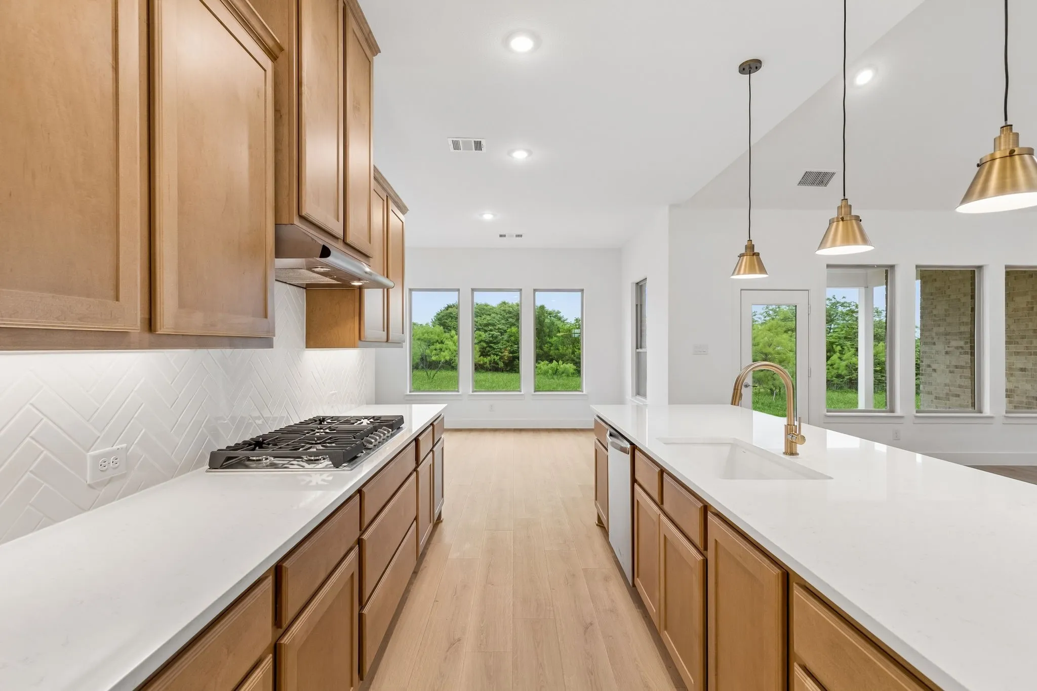 Kitchen featuring light wood-finish cabinetry, white countertops, herringbone tile backsplash, and a gas range