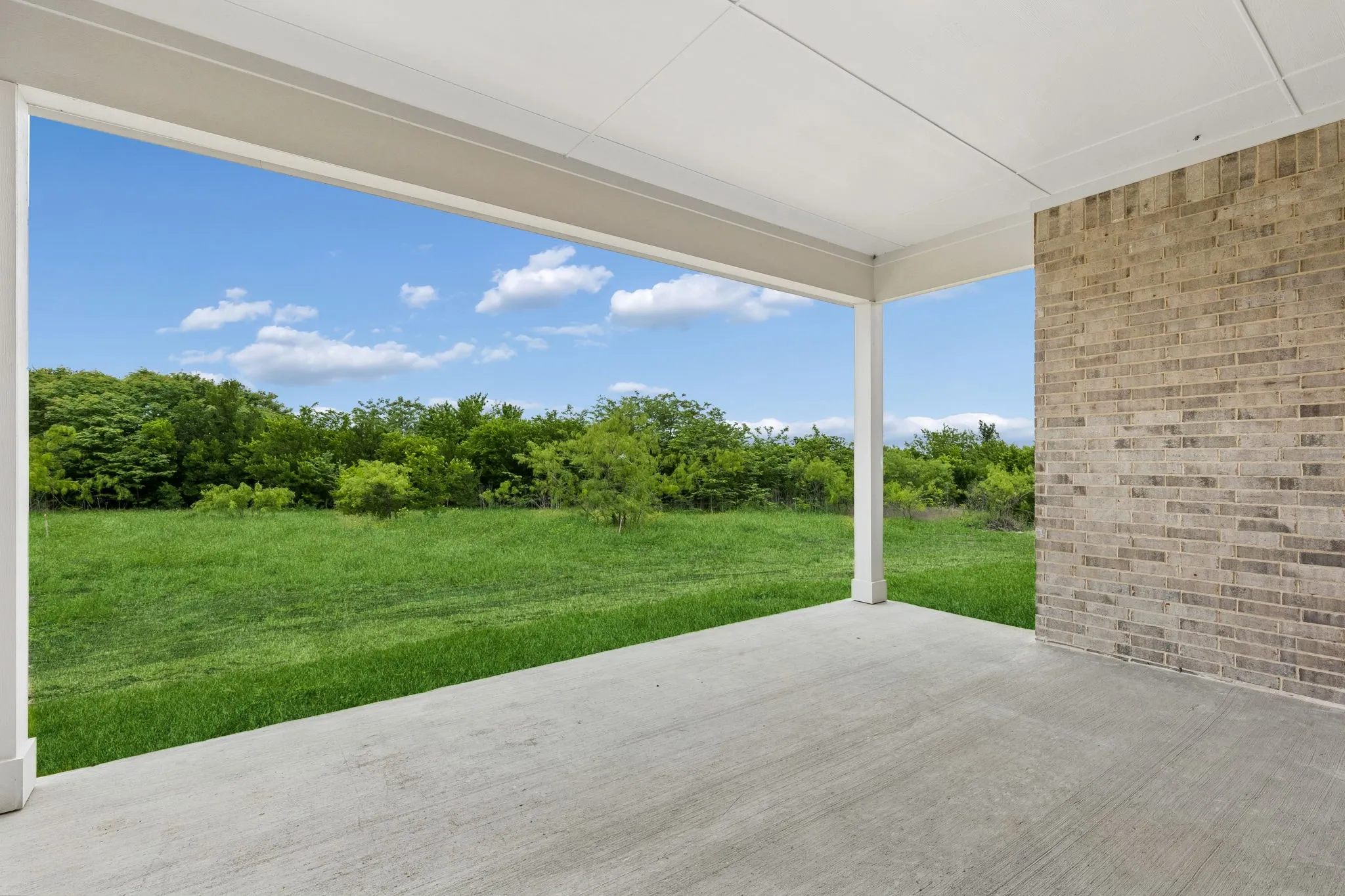 Covered concrete patio with a painted ceiling, supported by white columns, featuring a brick exterior wall