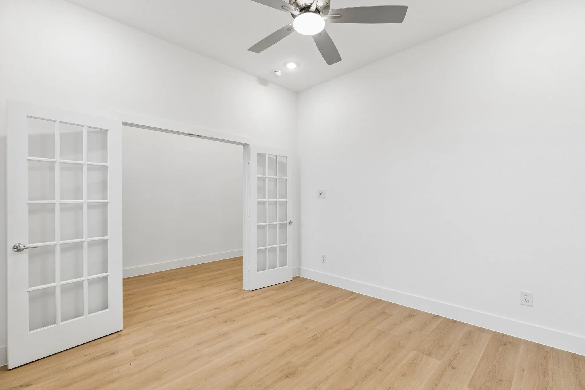 Wood-finish flooring, white walls, double French doors, ceiling fan with integrated lighting, and recessed lighting