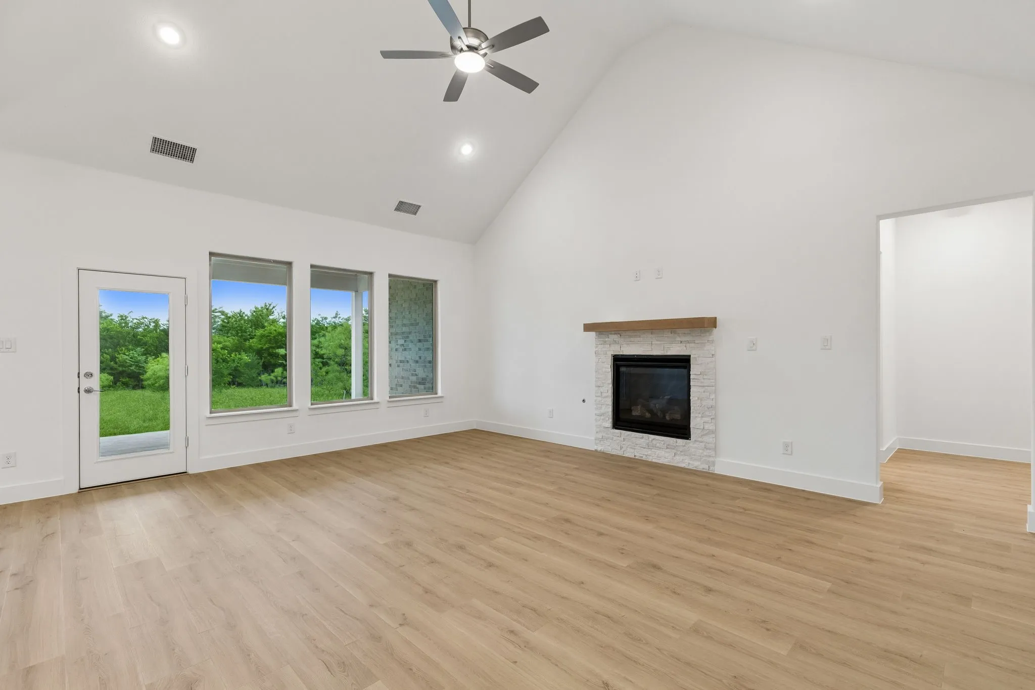 Vaulted ceiling with recessed lighting, ceiling fan, wood-finish flooring, and a fireplace with a stone surround and wood mantel