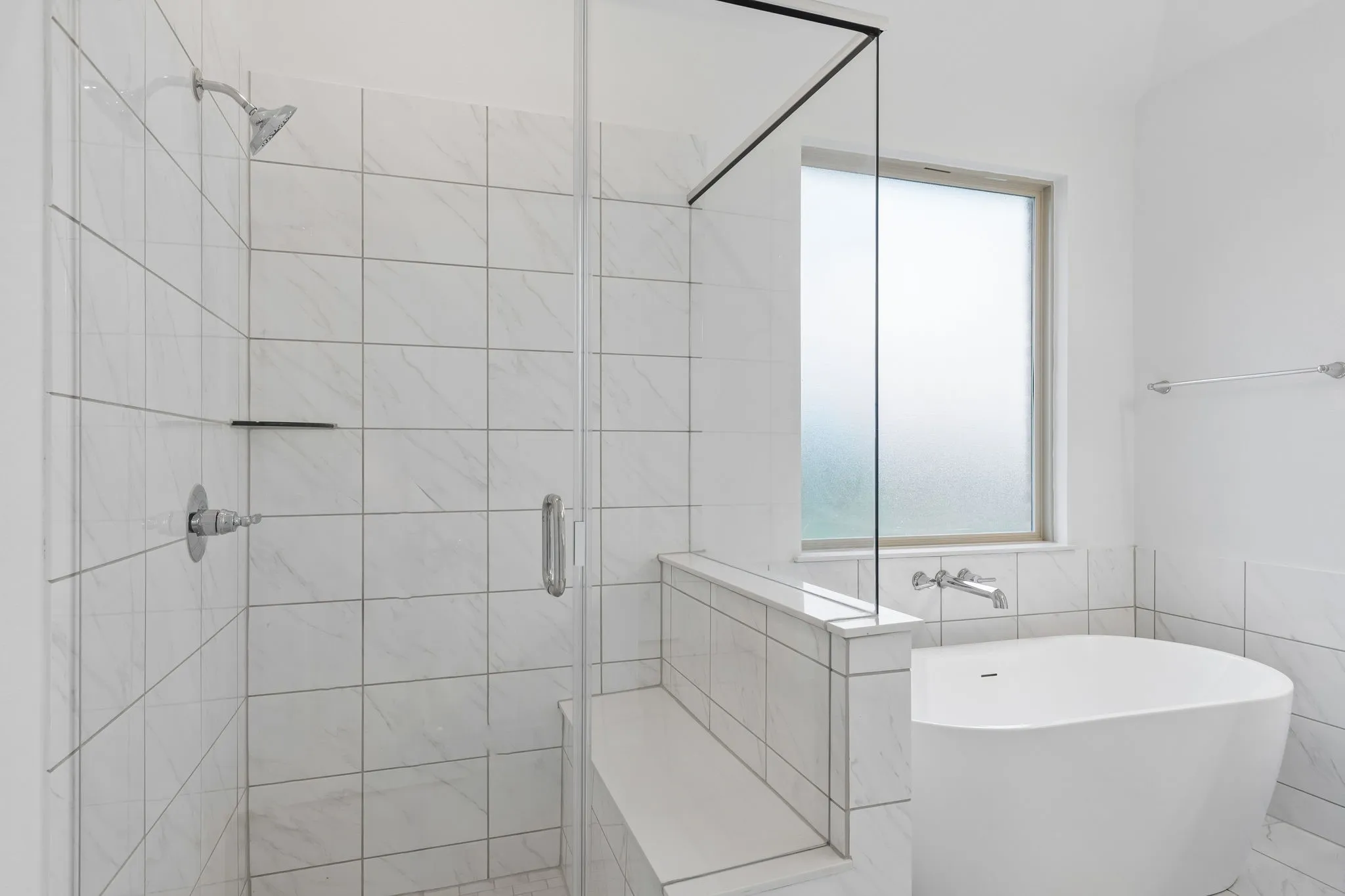 Walk-in shower with clear glass enclosure and integrated bench, chrome fixtures, and white tile surround