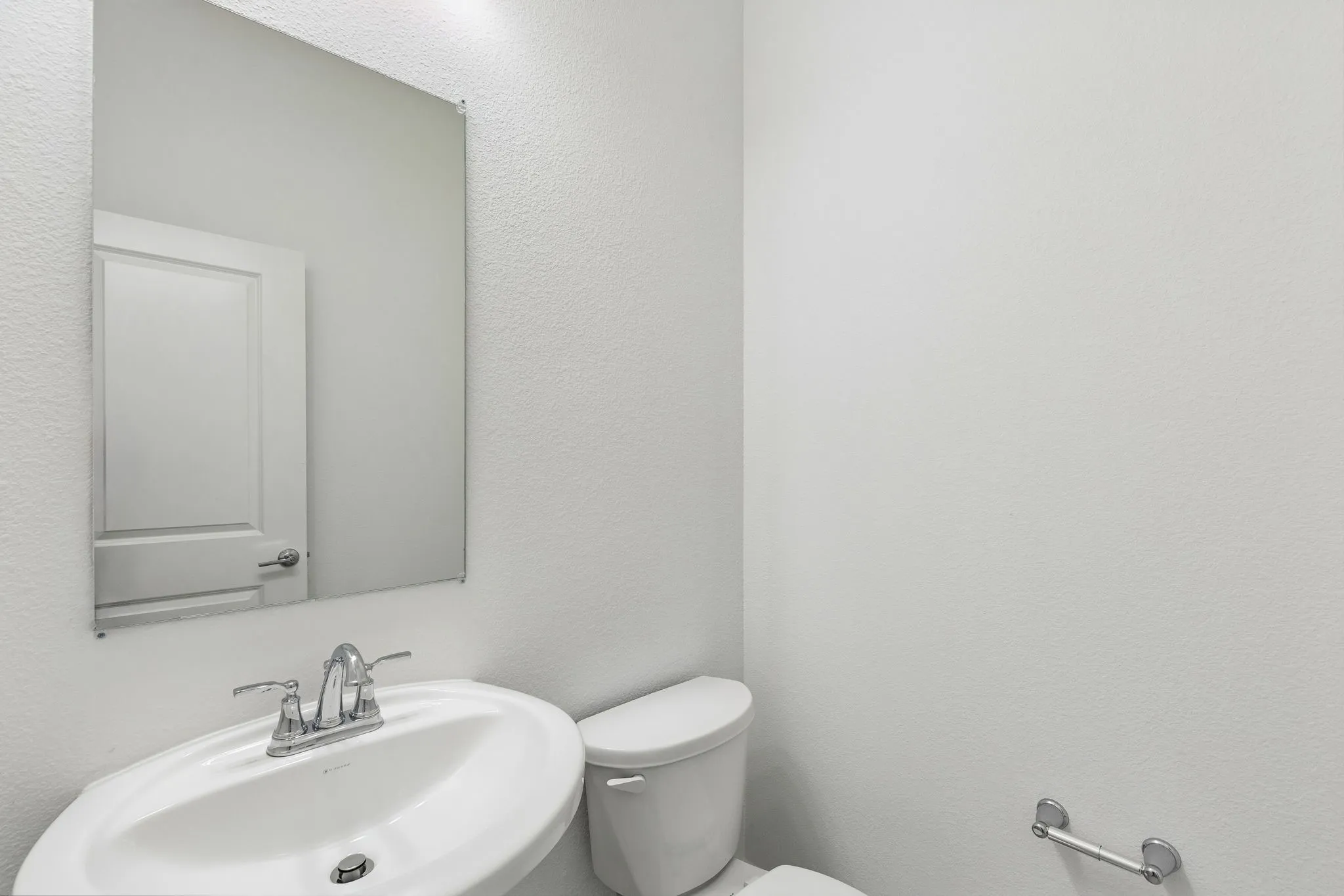 Wall-mounted mirror above a pedestal sink with a chrome two-handle faucet and a white toilet