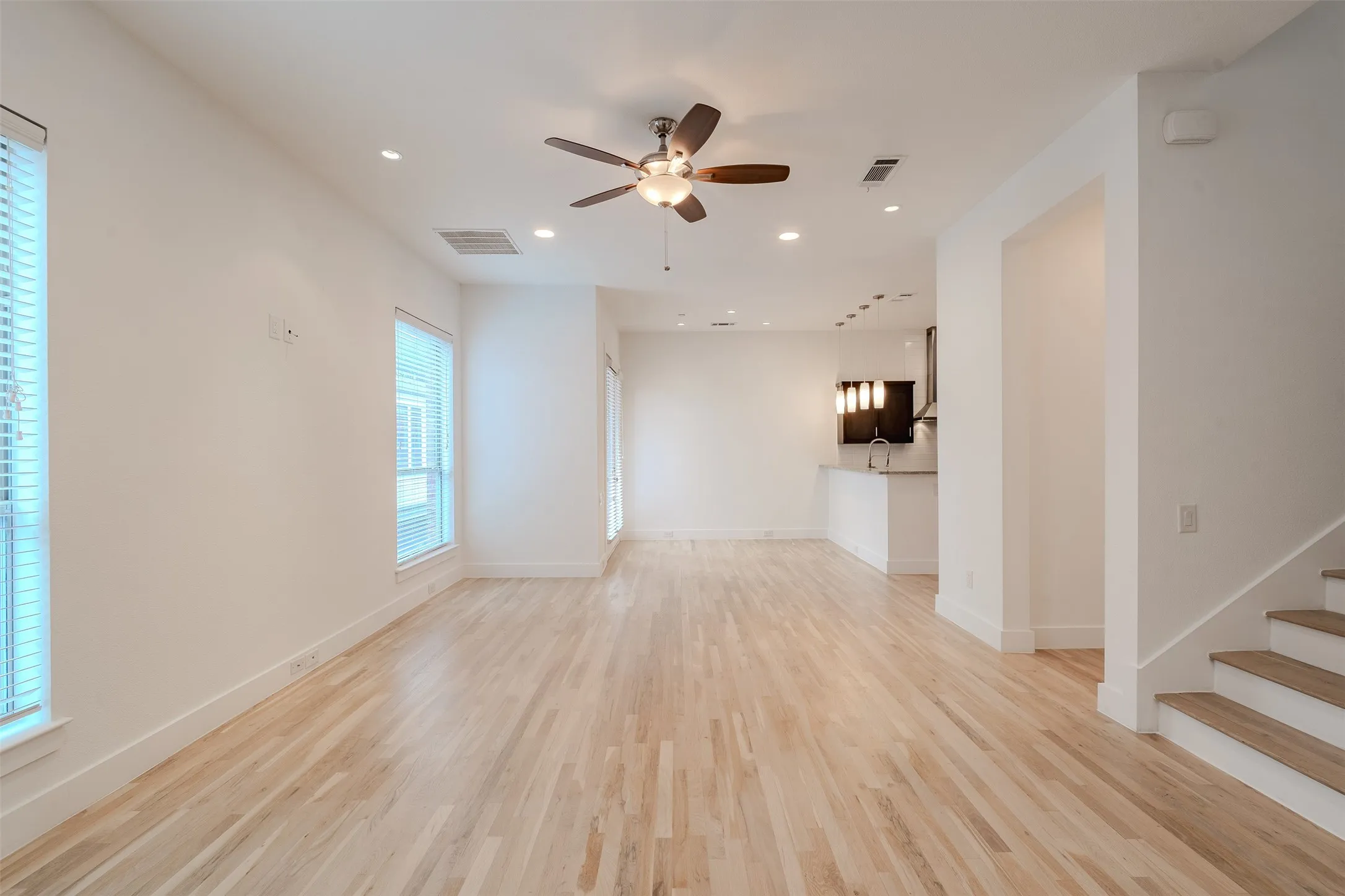 Open-concept living area with light wood-finish flooring, recessed lighting, and a ceiling fan