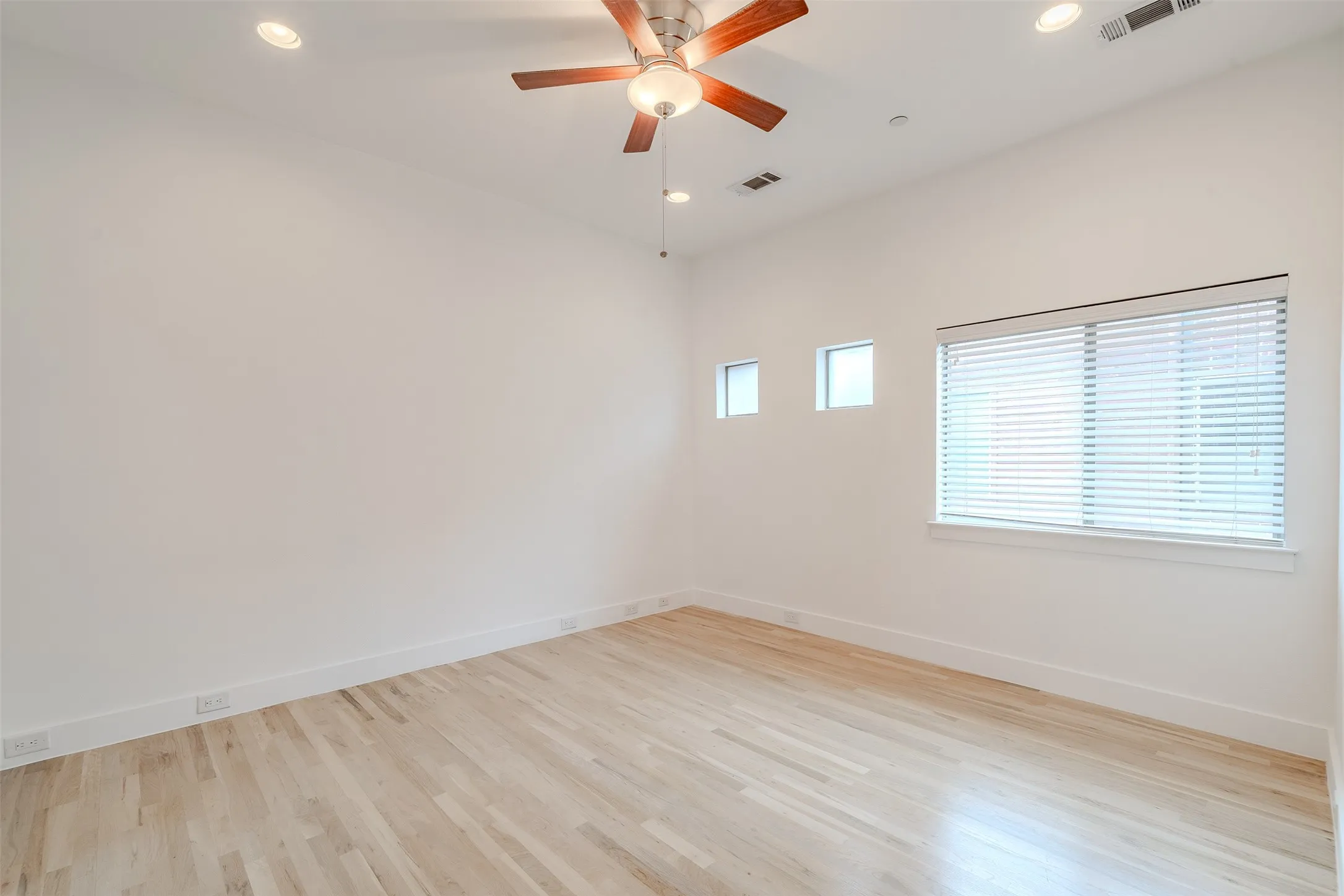Wood-finish flooring, recessed lighting, ceiling fan, multiple windows, and white walls