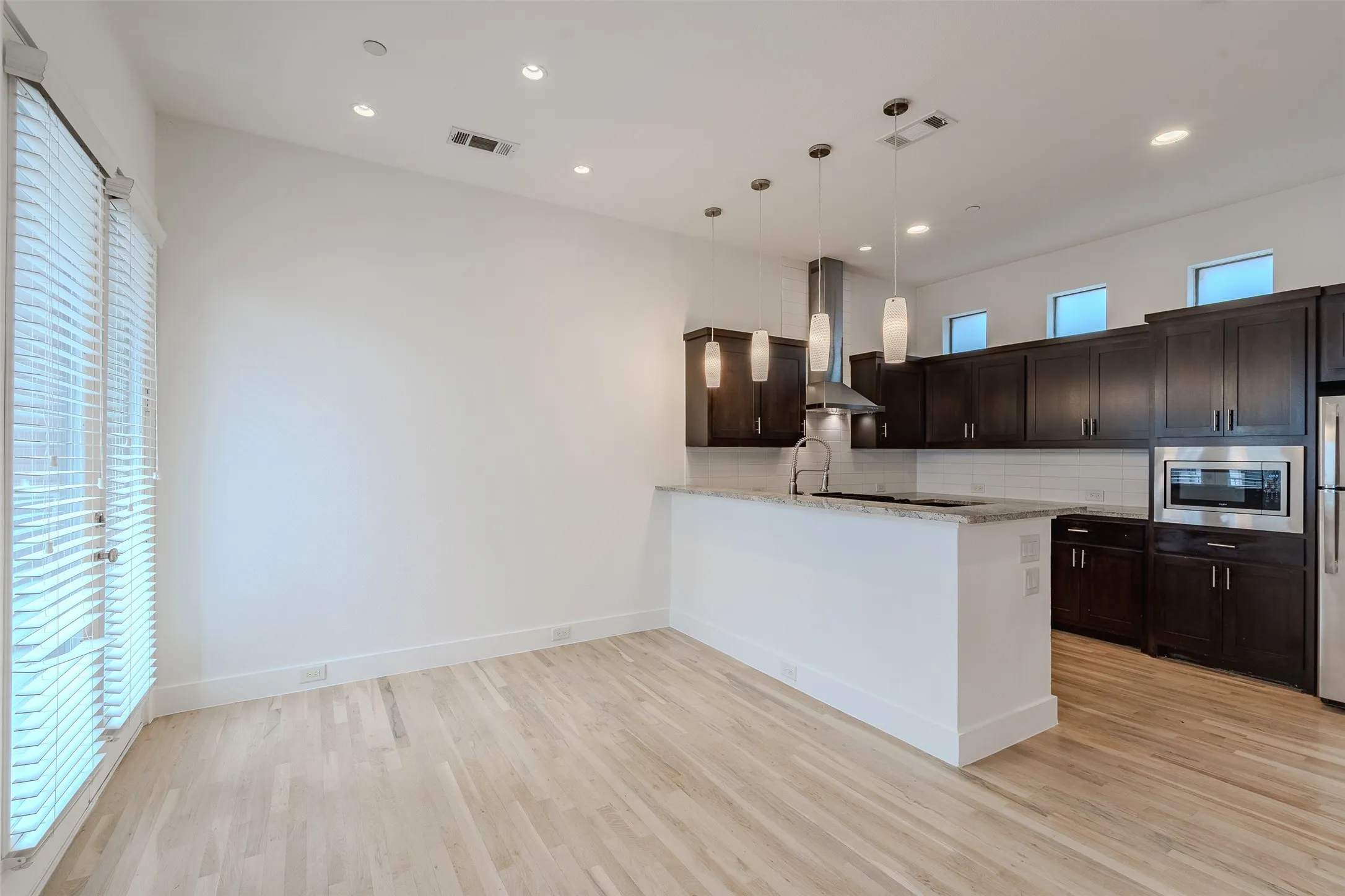 Open-concept kitchen featuring dark wood cabinetry, stainless steel appliances, a center island with a stone countertop, and light wood-finish flooring