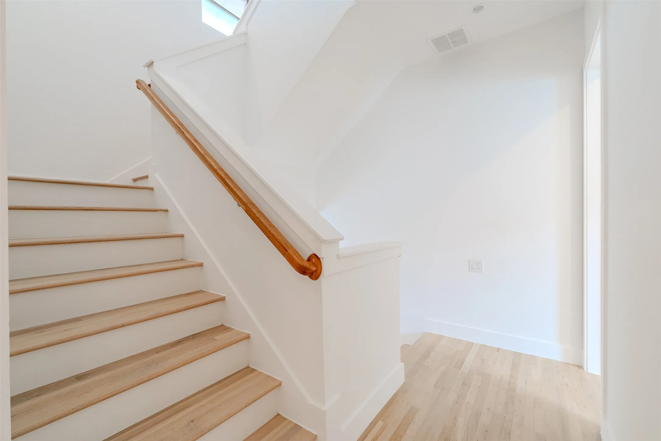 Staircase featuring wood treads, white risers, a light wood handrail, and white wall finishes