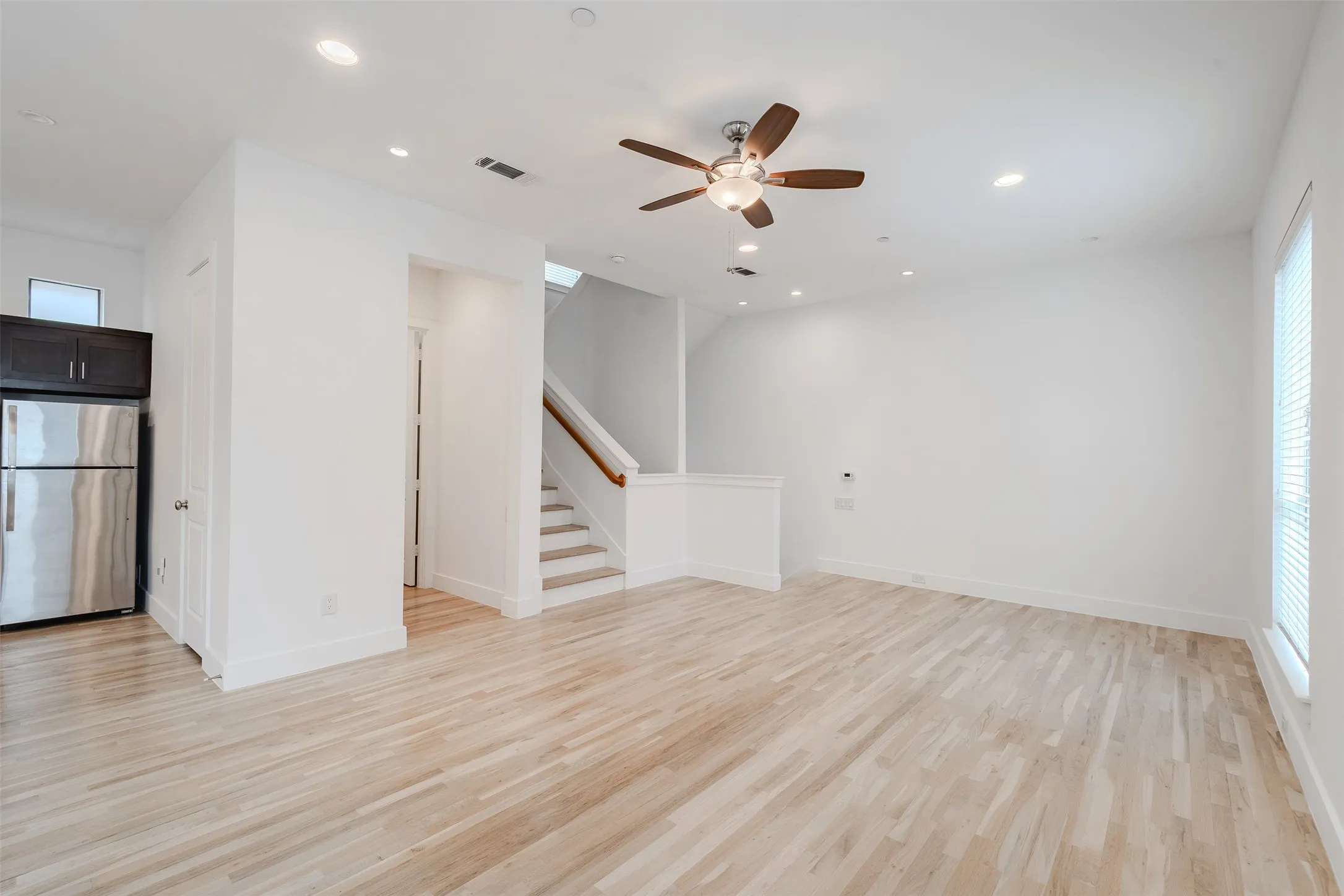 Expansive open-concept room featuring wood-finish flooring, a ceiling fan with integrated lighting, recessed lighting, and a stainless steel refrigerator