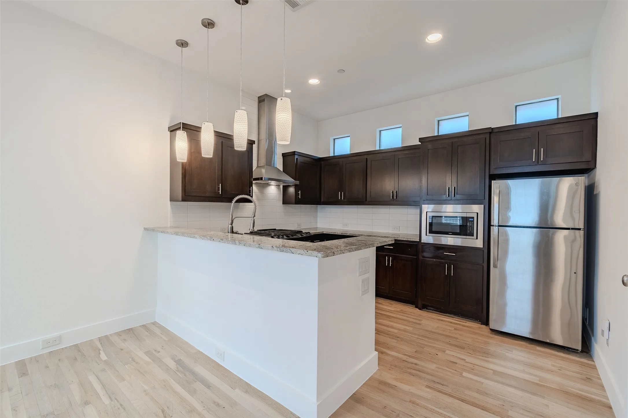 Kitchen featuring wood-finish flooring, dark wood cabinetry, stainless steel appliances, and a breakfast bar with stone countertops