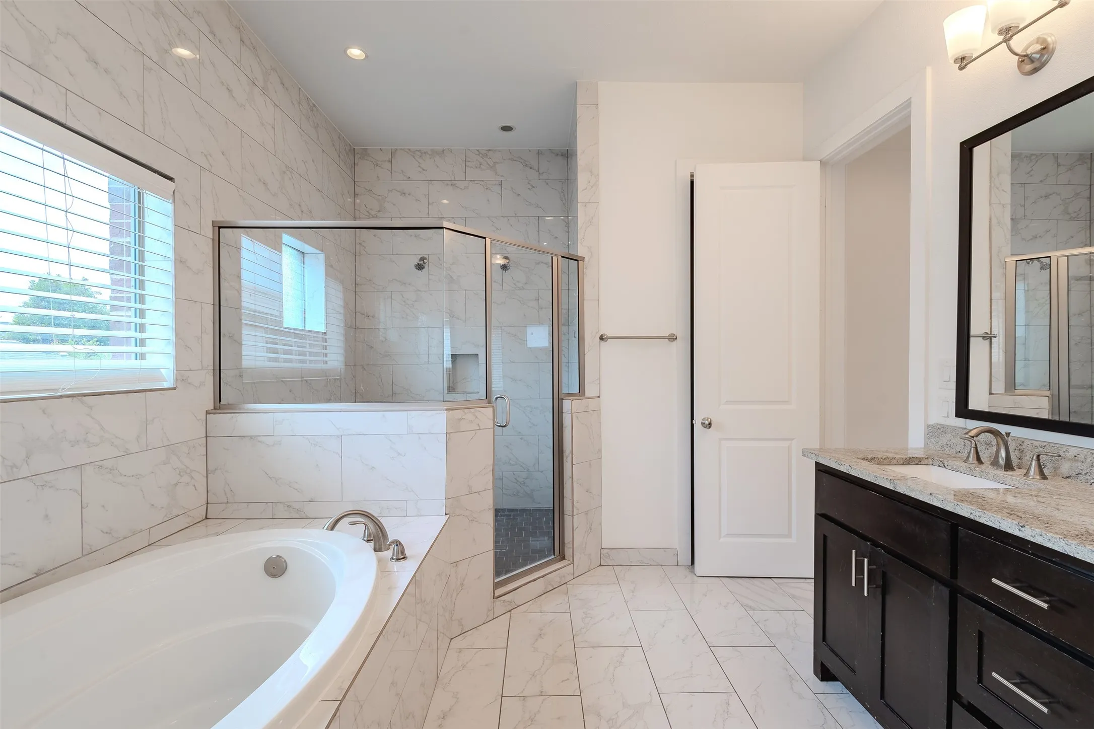 Walk-in shower with glass enclosure, separate soaking tub, double vanity with stone countertop, and tile flooring