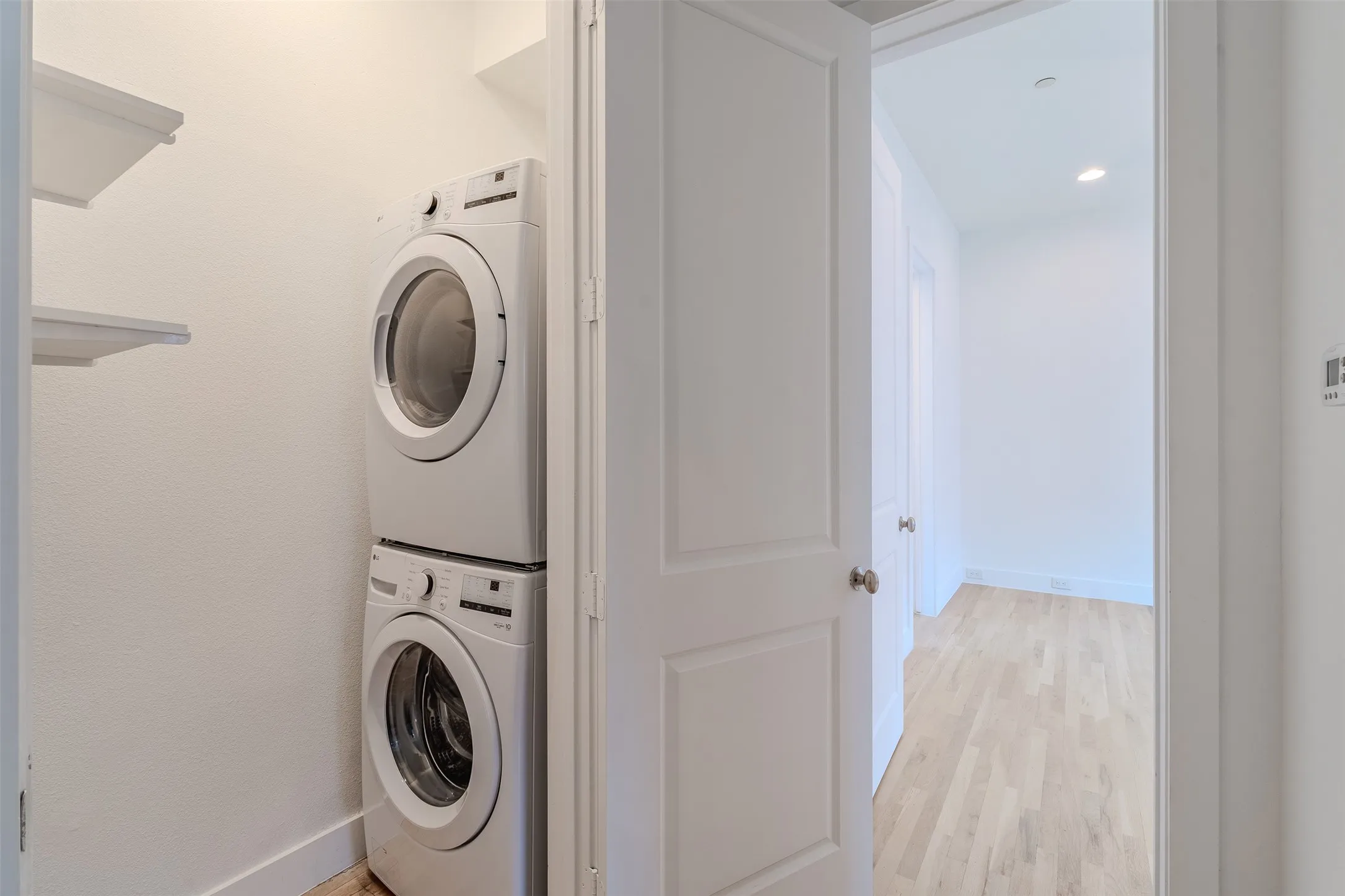 Stackable laundry appliances, wall-mounted shelving, solid core interior door, and wood-finish flooring
