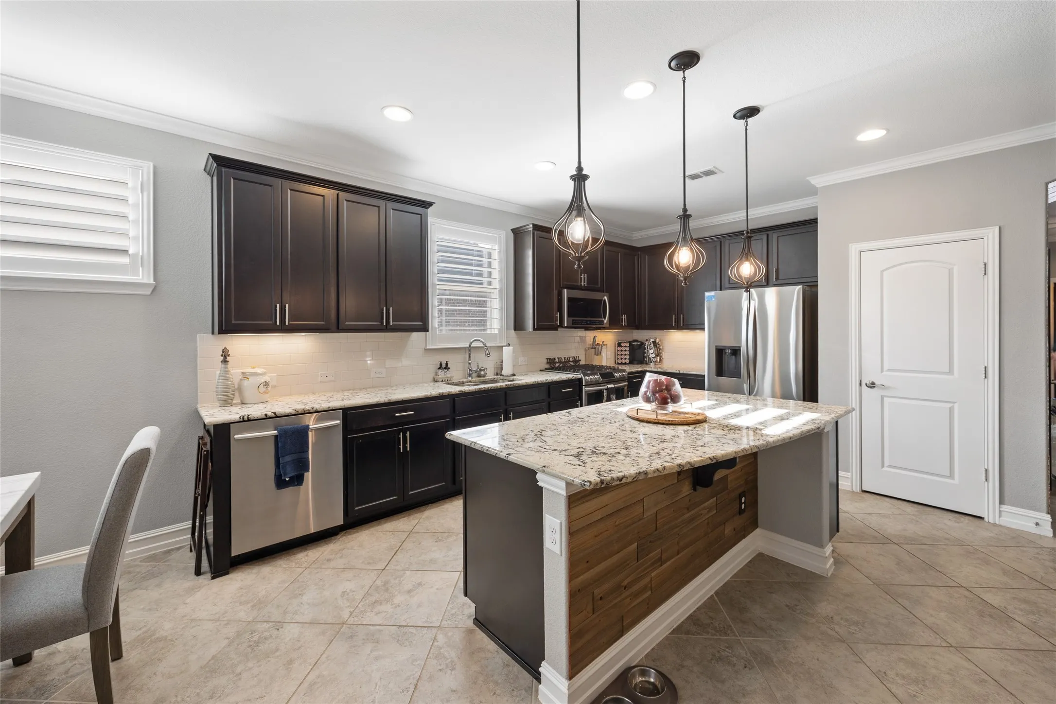 Kitchen featuring dark wood cabinetry, light-toned granite countertops, tile flooring, a center island with a wood panel accent, and recessed lighting