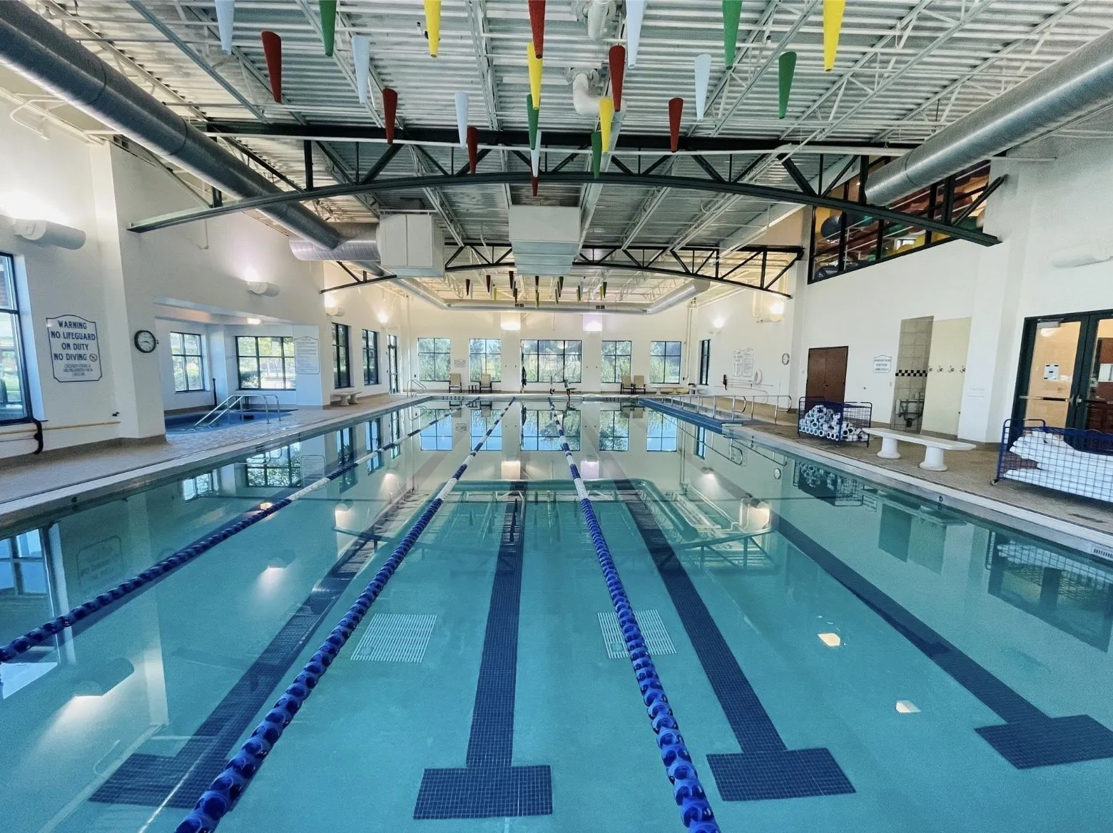 Indoor lap pool with multiple lanes, high ceilings, large windows, and exposed structural beams