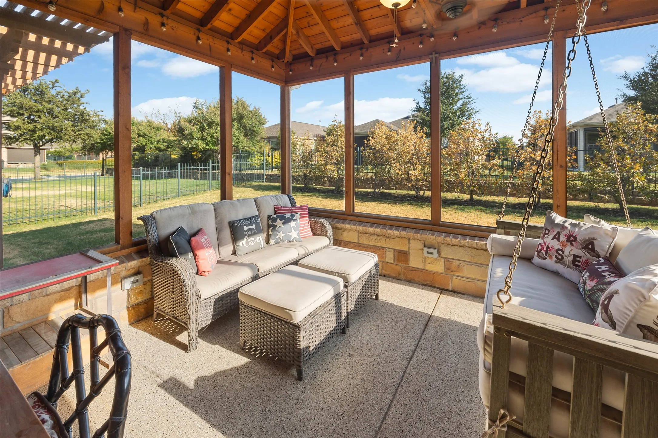 Screened outdoor structure featuring a vaulted wood-beam ceiling, exposed aggregate concrete flooring, and a stone half-wall