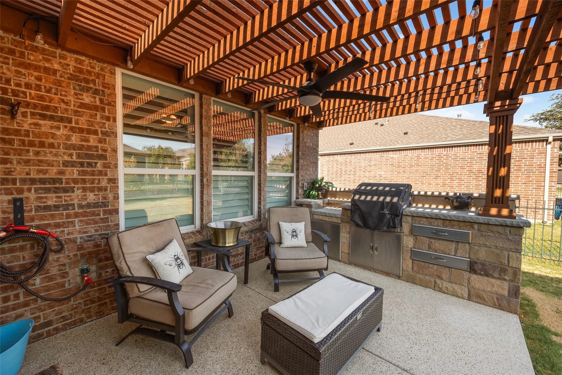 Patio with wood pergola, built-in outdoor kitchen, ceiling fan, and brick exterior
