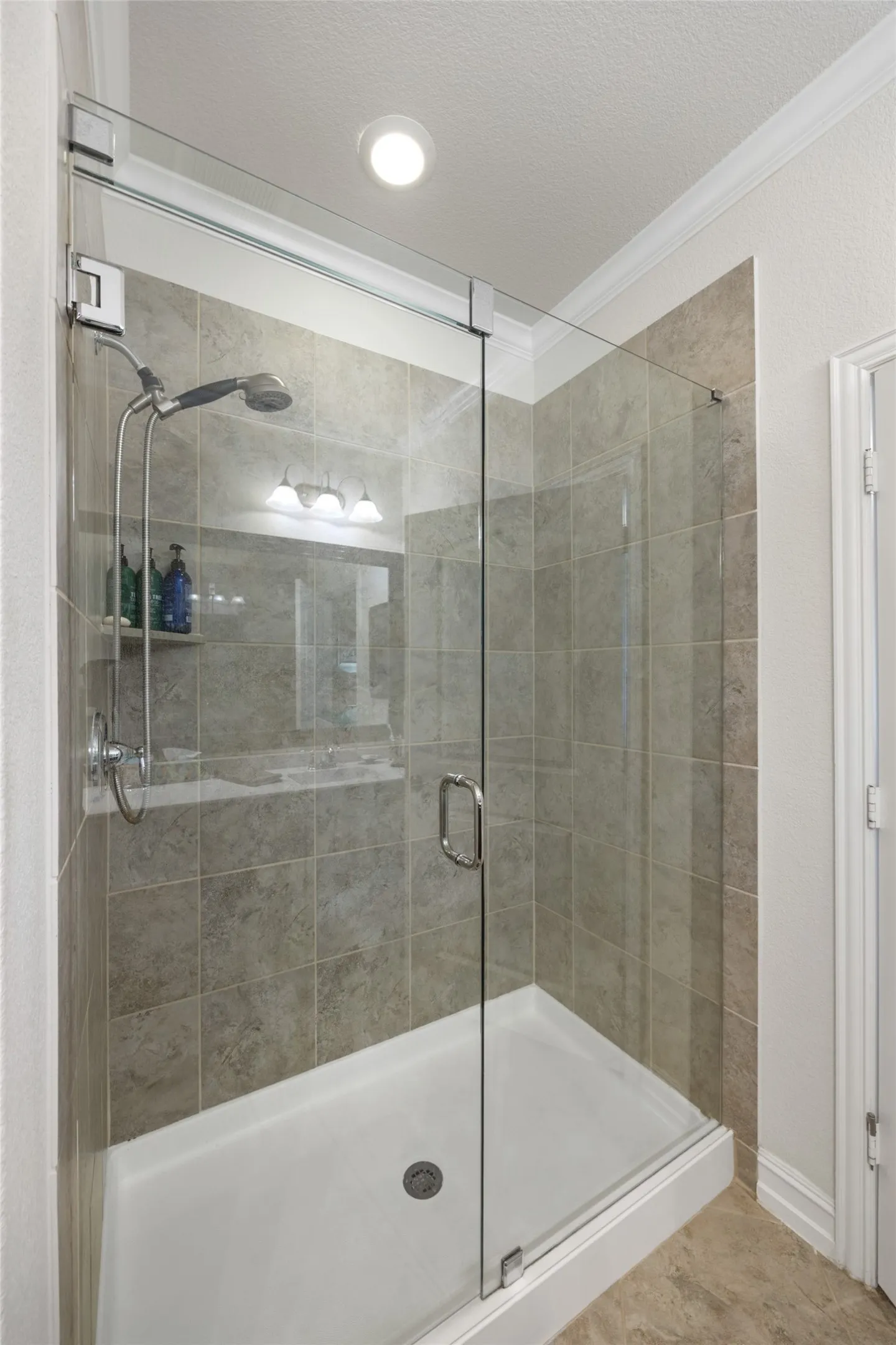 Glass-enclosed shower with a handheld showerhead, tiled walls, and a recessed ceiling light