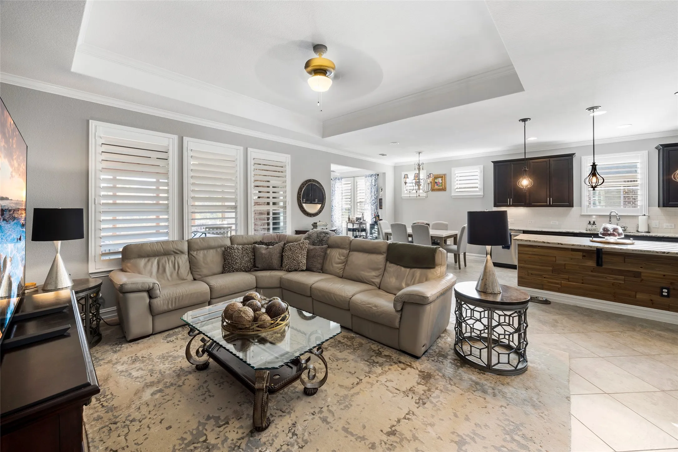 Tray ceiling with crown molding, plantation shutters, recessed lighting, tile flooring, and dark wood cabinetry