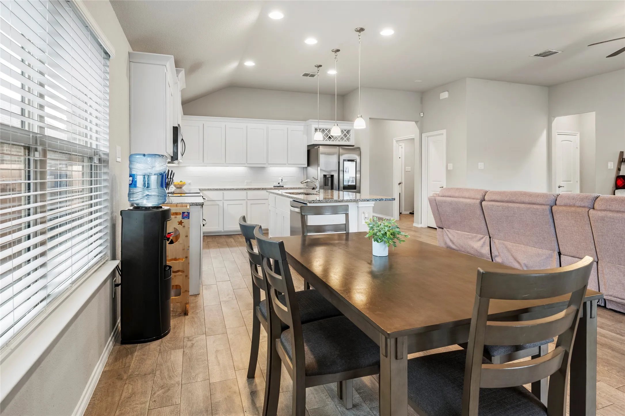 Open-concept kitchen and dining area with wood-like flooring, white cabinetry, and stainless steel appliances