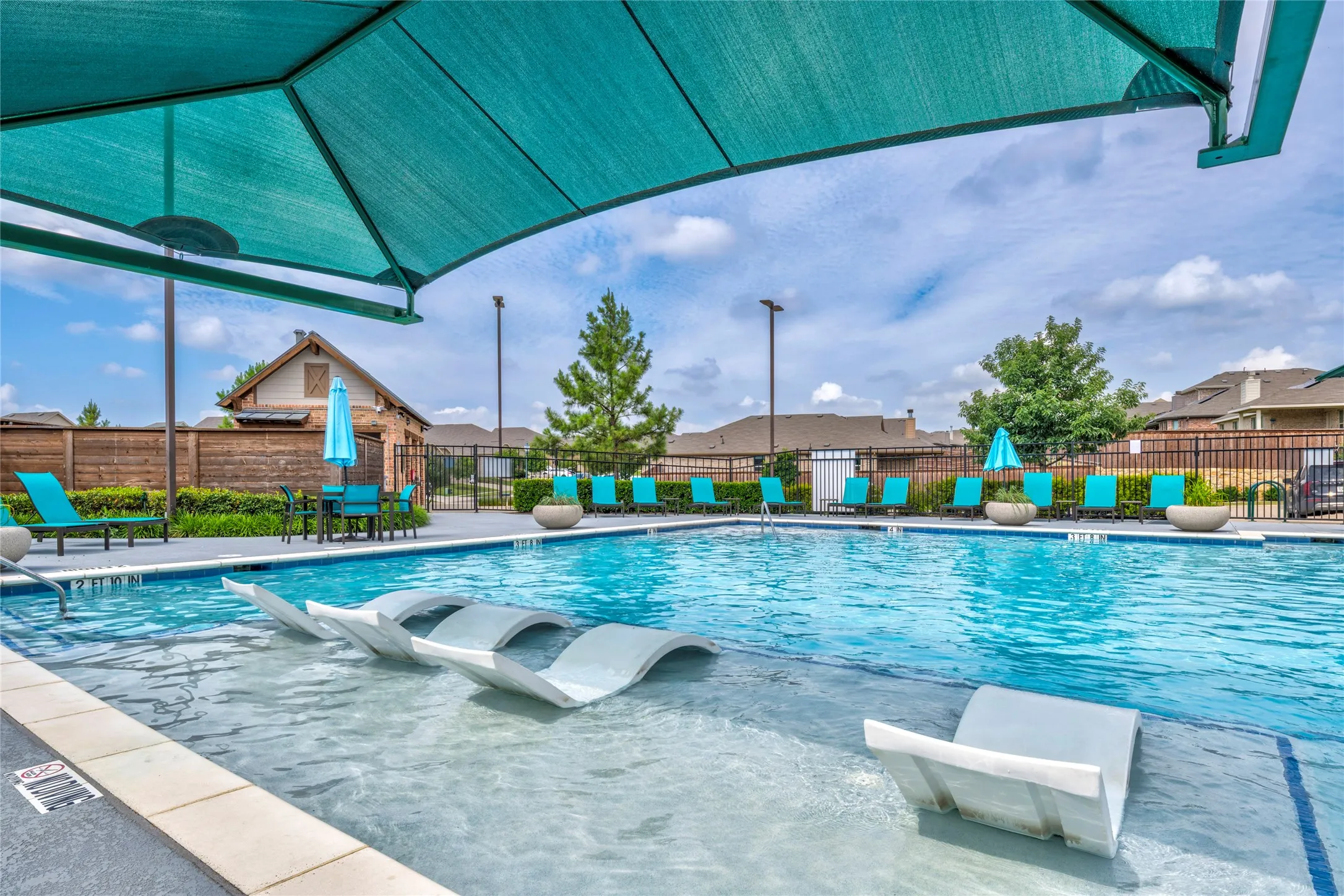 Swimming pool with an integrated tanning ledge, shaded lounge area, and perimeter fencing