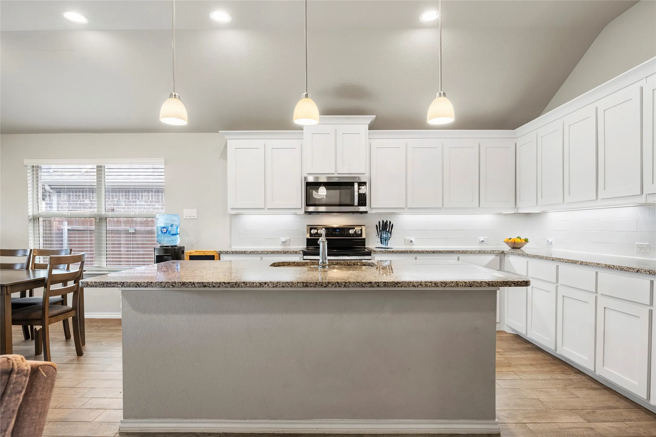 Great sized kitchen featuring vaulted ceilings, white shaker cabinetry, granite countertops, wood-finish flooring, and recessed lighting...