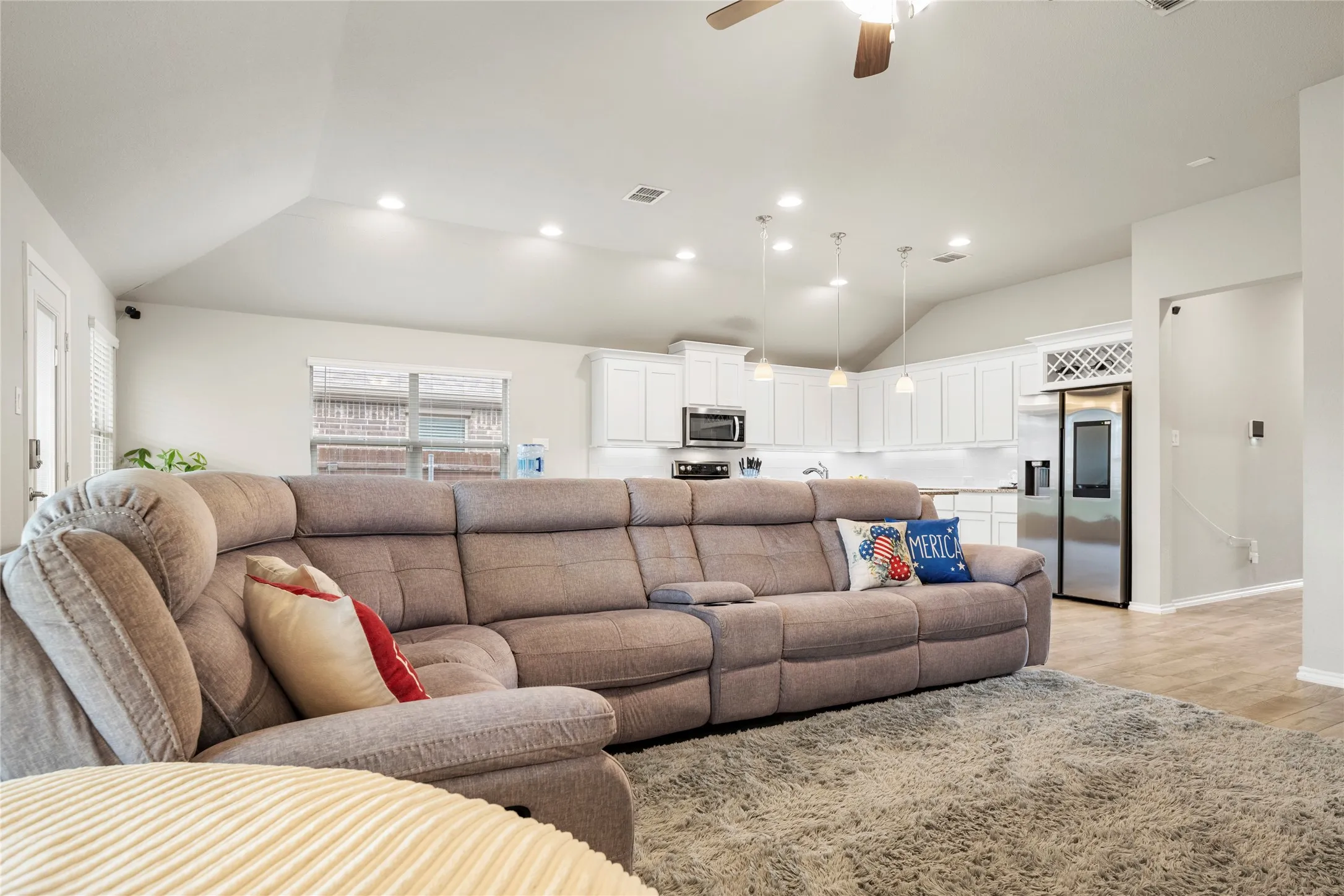 Vaulted ceilings with recessed lighting, kitchen with white cabinetry, stainless steel appliances, and wood-finish flooring