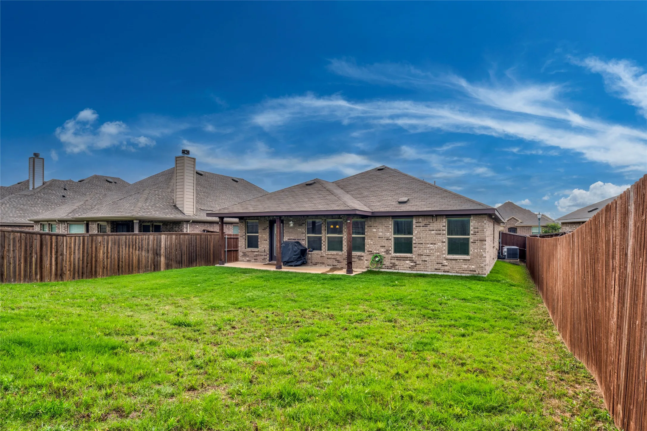 Expansive grassy yard with wood fencing, a covered patio, and brick exterior