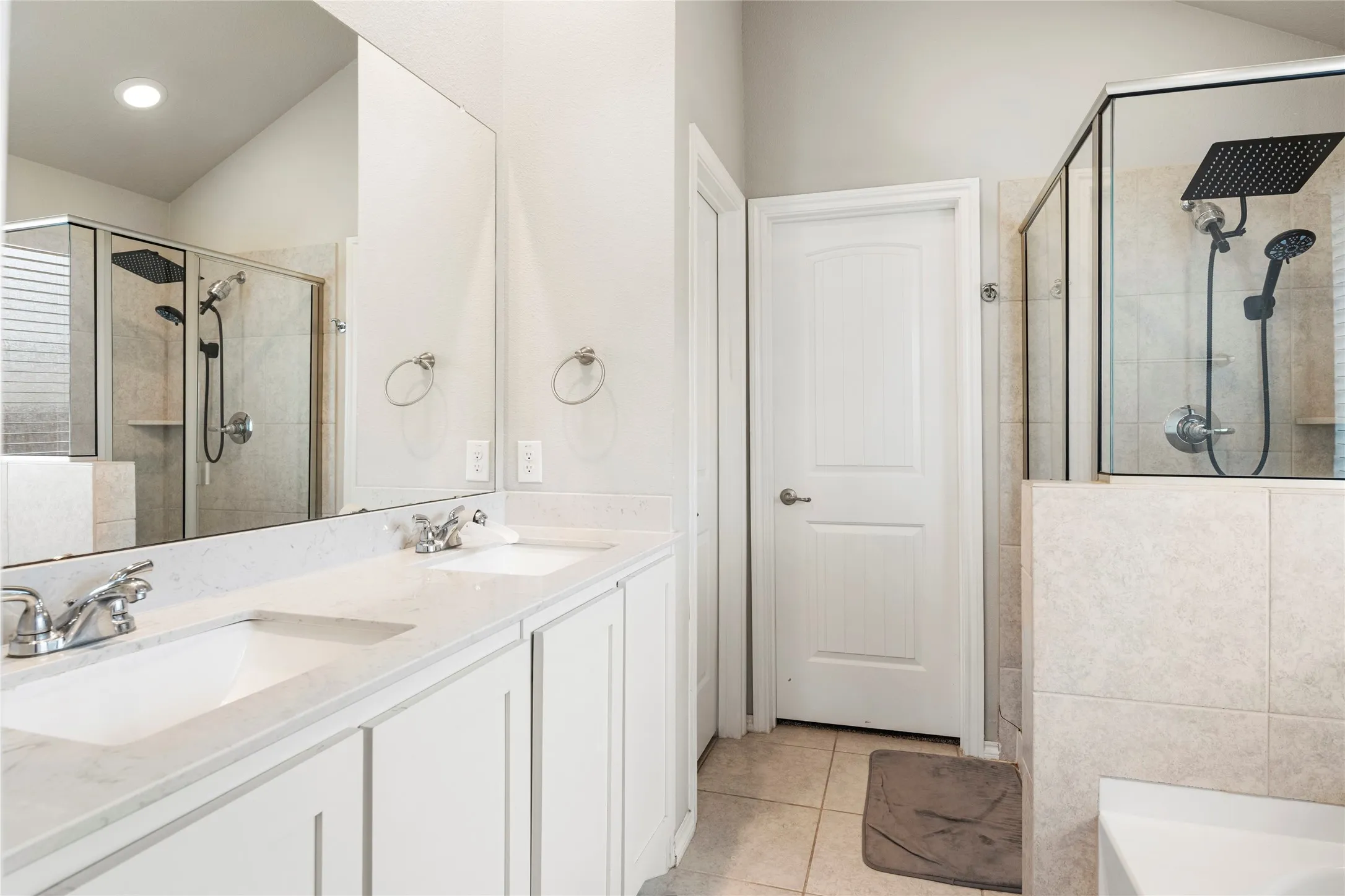 Dual vanity with integrated sinks and chrome fixtures, framed mirror, and a glass-enclosed shower with a rainfall showerhead