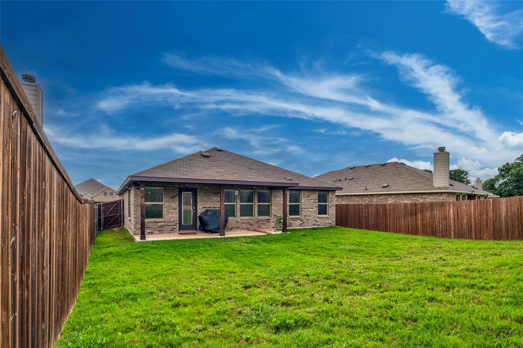 Expansive grassy yard with full fencing, a covered patio, and brick exterior