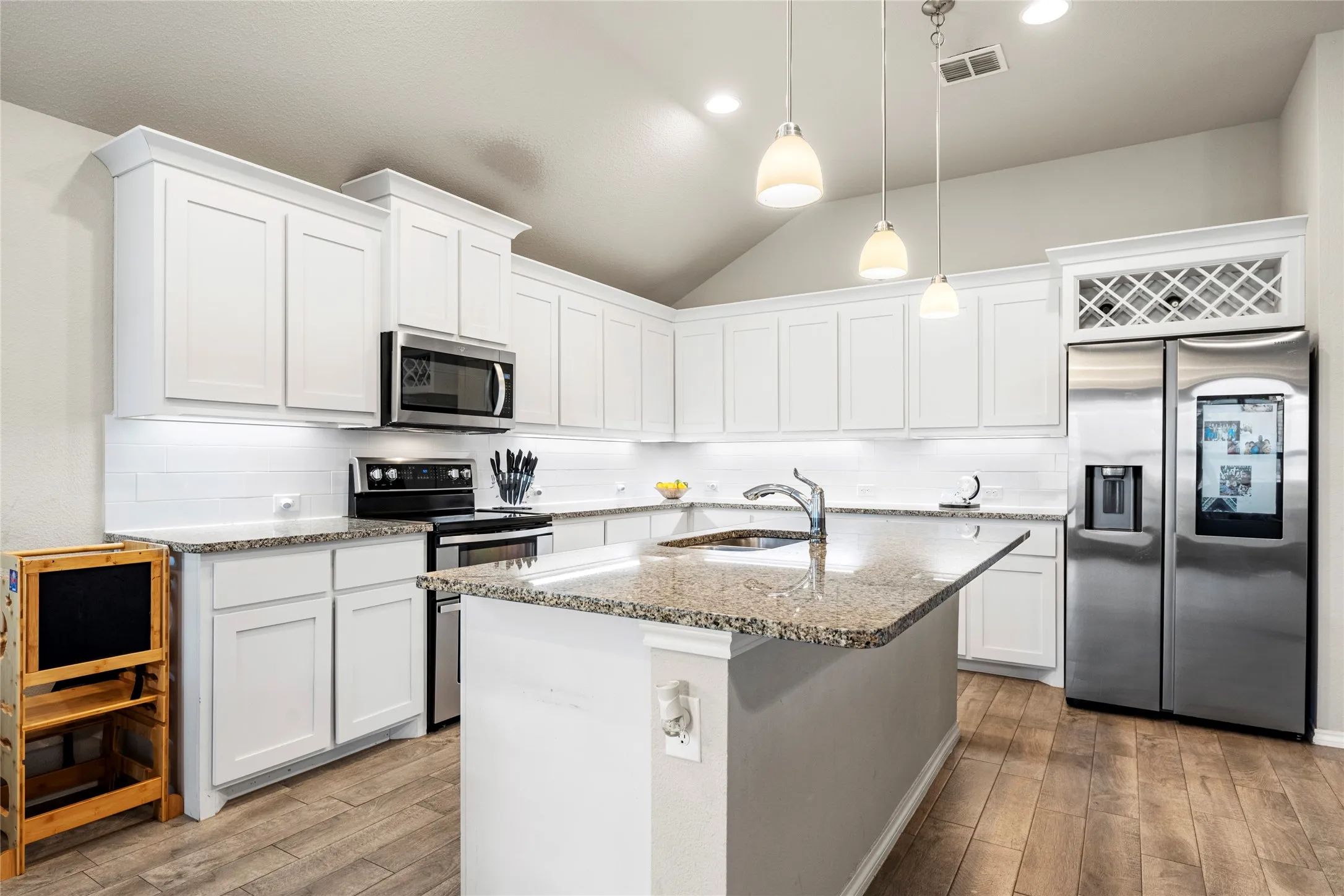 Kitchen featuring white cabinetry, granite countertops, stainless steel appliances, wood-finish flooring, and a vaulted ceiling (does not include refrigerator).