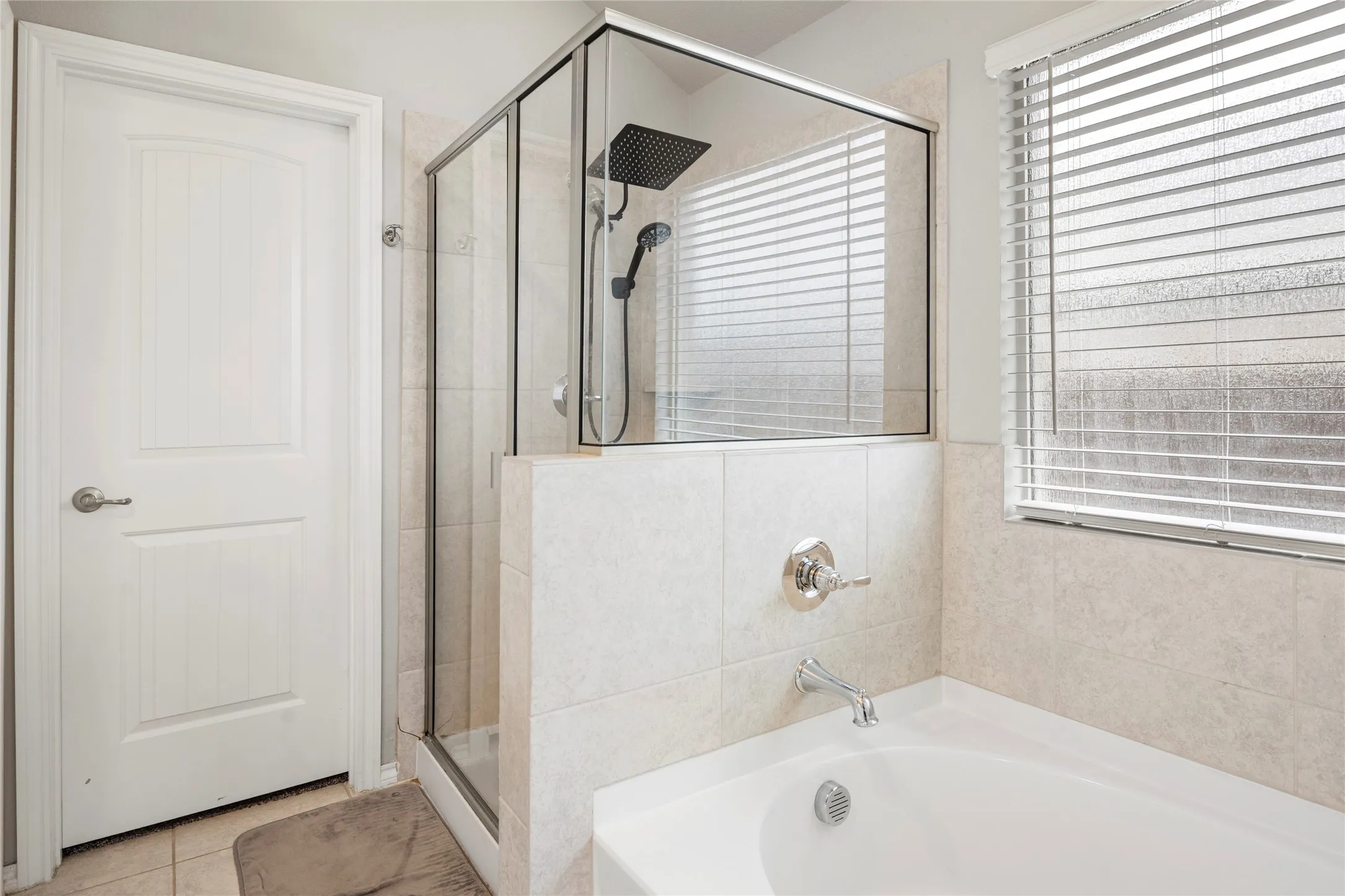 Enclosed glass shower with rain showerhead, separate soaking tub, and tiled surrounds